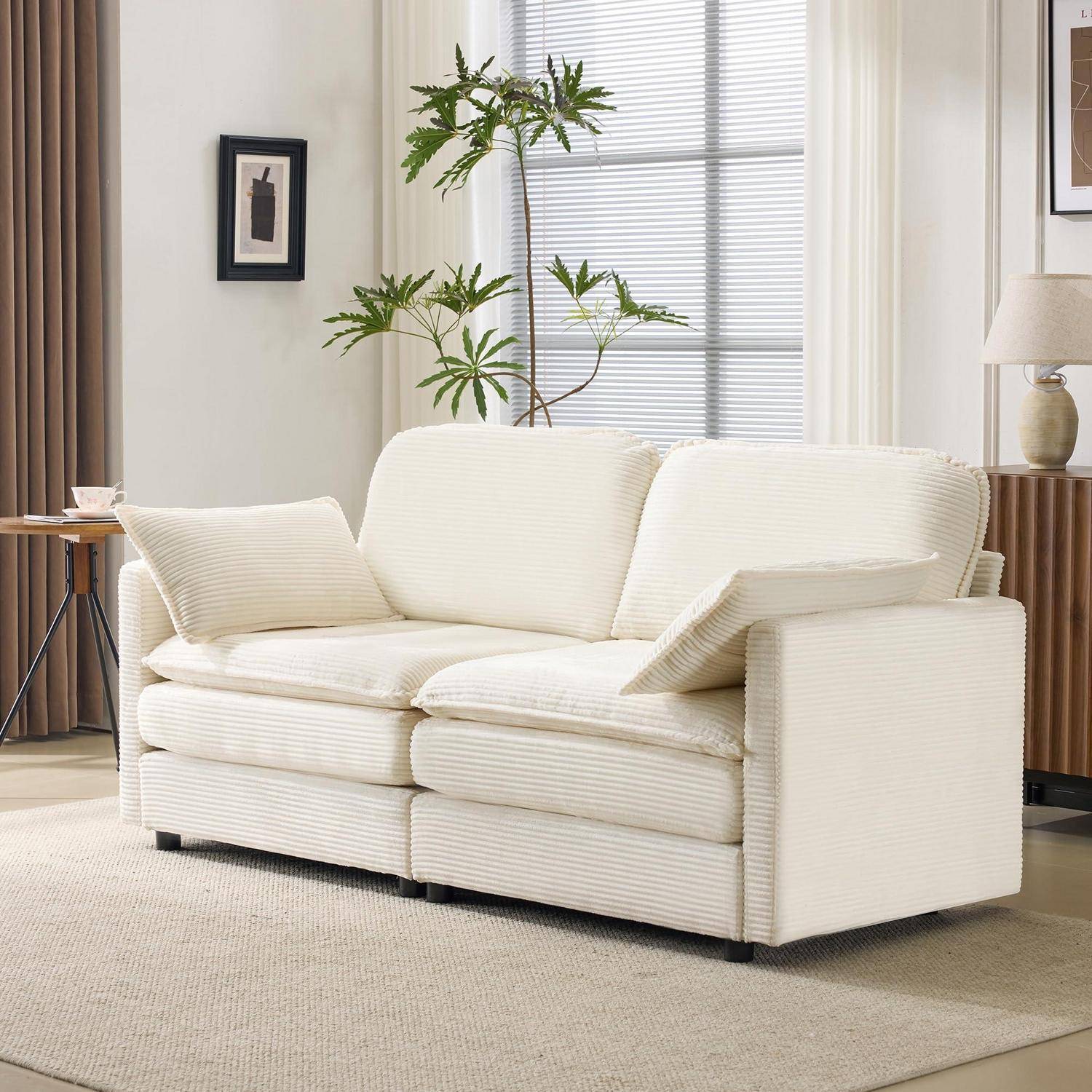 Creme-gestreiftes Sofa mit Kissen in einem hellen Wohnzimmer, auf einem beigen Teppich neben einem Fenster und einer Zimmerpflanze.