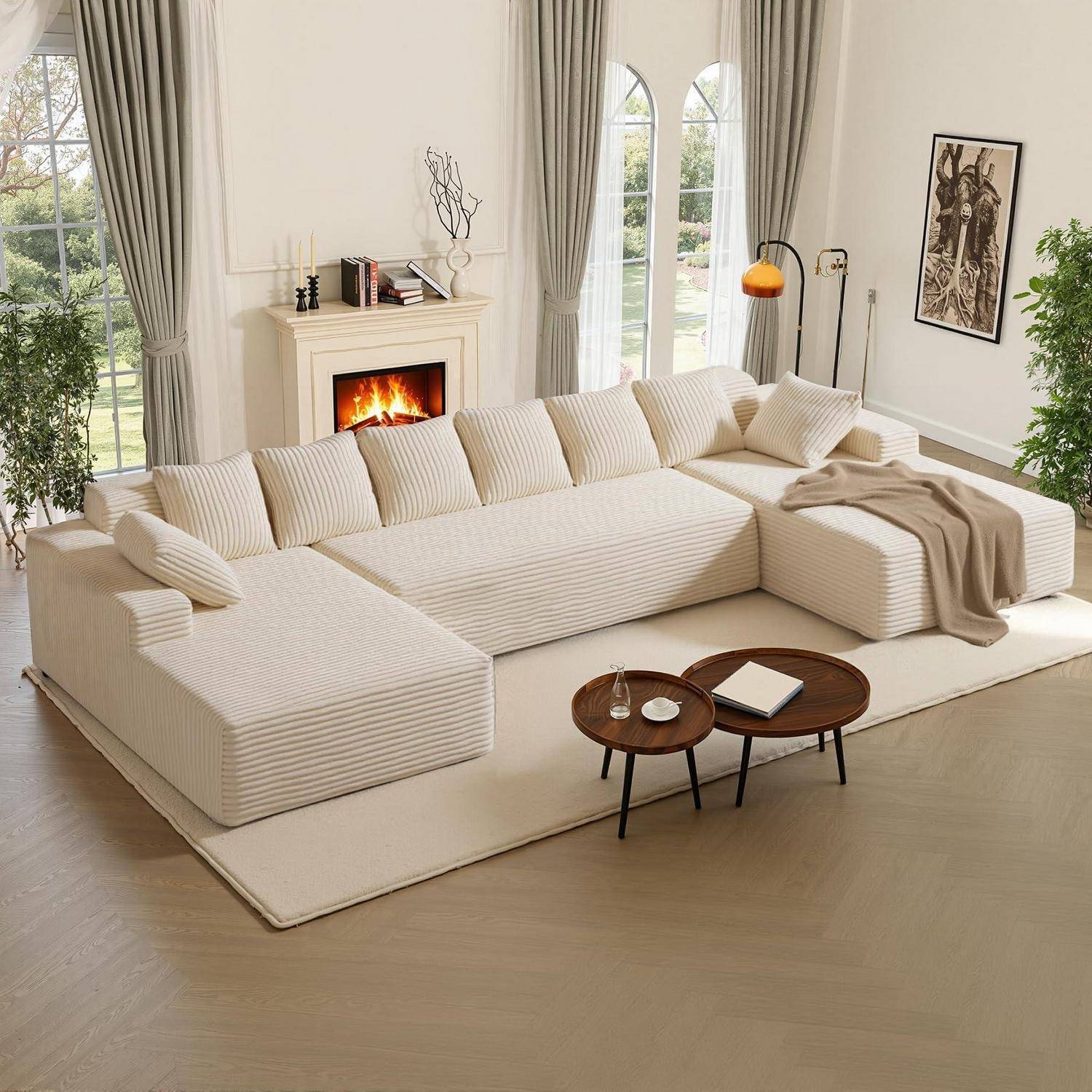 Helles Wohnzimmer mit einem großen cremefarbenen Ecksofa, Kamin, hohen Fenstern und zwei runden Couchtischen davor.