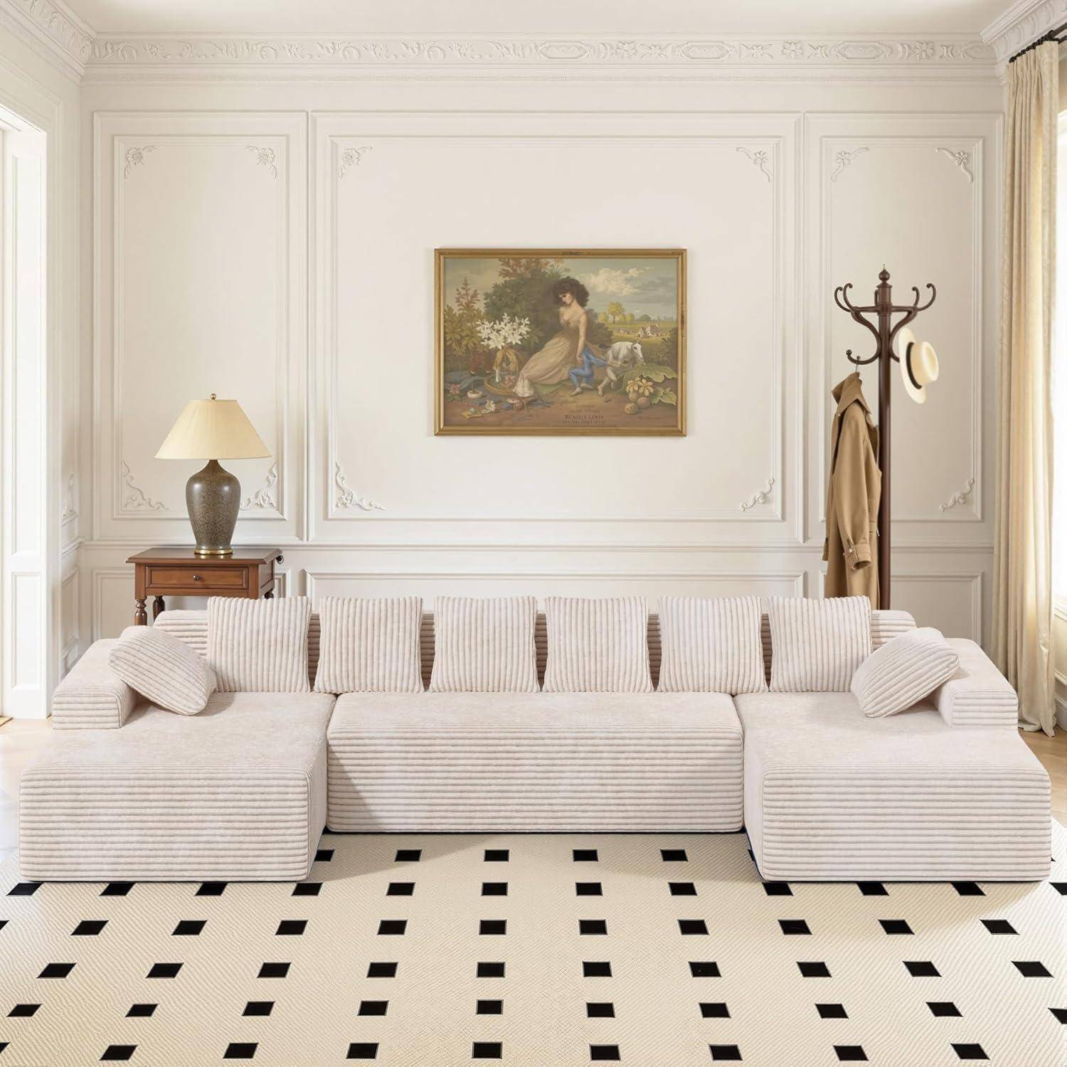 Helles Wohnzimmer mit cremefarbigem Ecksofa, Garderobe, Lampe, gerahmter Wandkunst und weißem Teppich mit schwarzem Quadratmuster.
