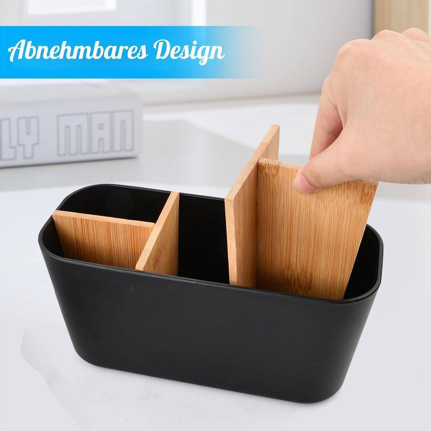 Hand, die einen Bamboo-Teiler in einen schwarzen Aufbewahrungsorganizer auf einem weißen Tisch einsetzt, wobei modulare Fächer sichtbar sind.