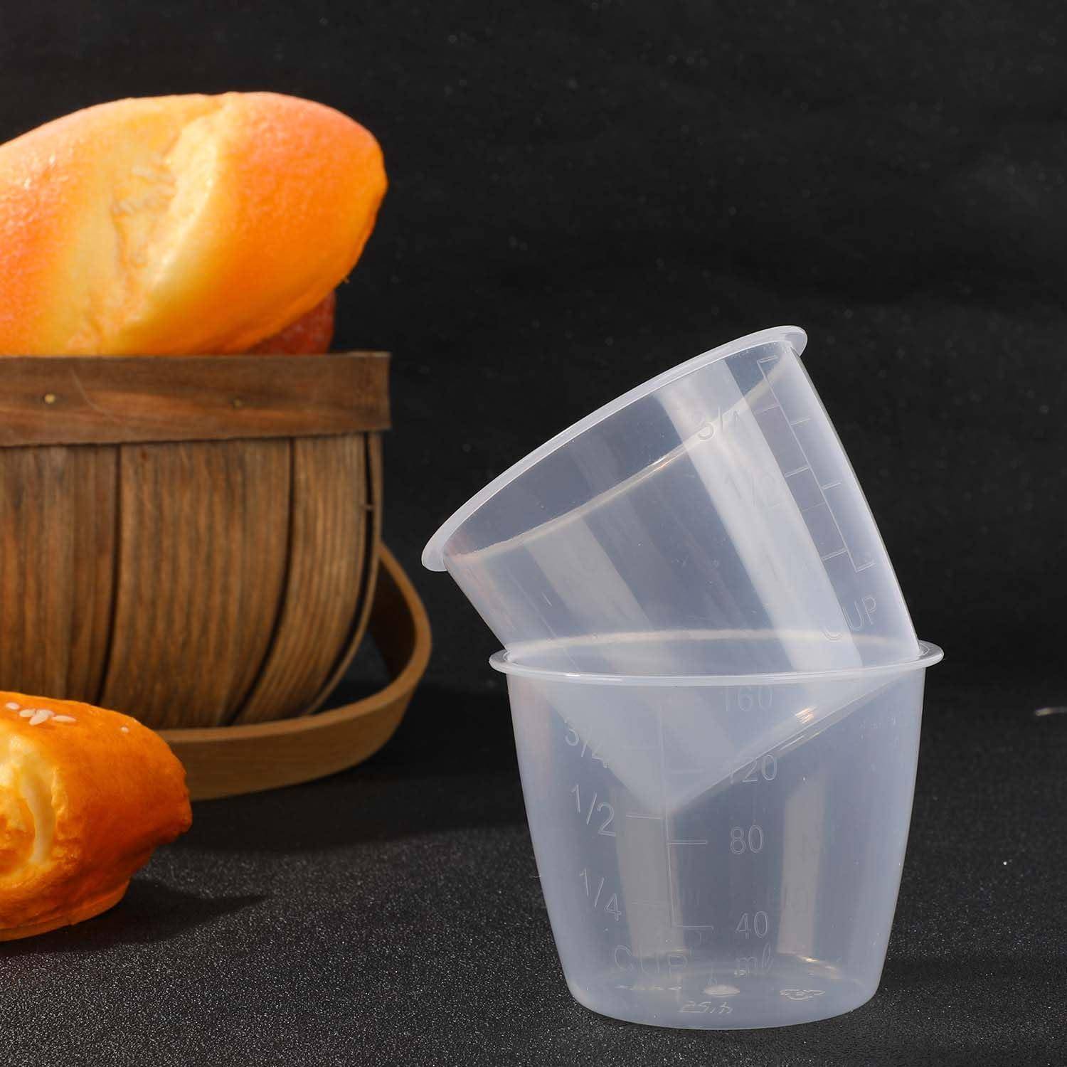 Zwei durchscheinende Kunststoff-Messbehälter, übereinander gestapelt, auf einer dunklen Oberfläche neben einem Holzkorb mit orangefarbigem Obst.