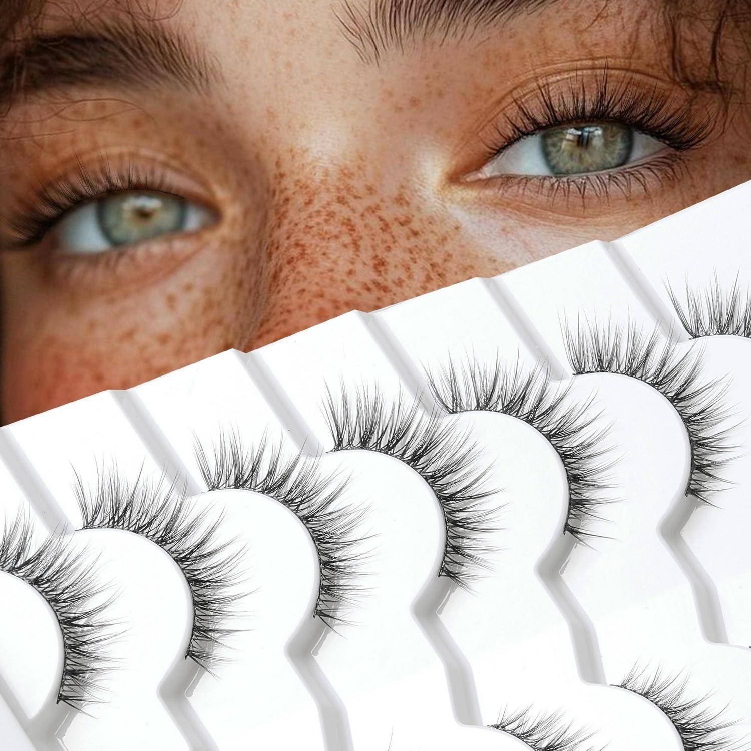 Nahaufnahme von sommersprössigen Augen über einem Fächer aus falschen Wimpern auf weißer Verpackung, was auf eine Wimpernverlängerung oder Schönheitsproduktbewerbung hindeutet.