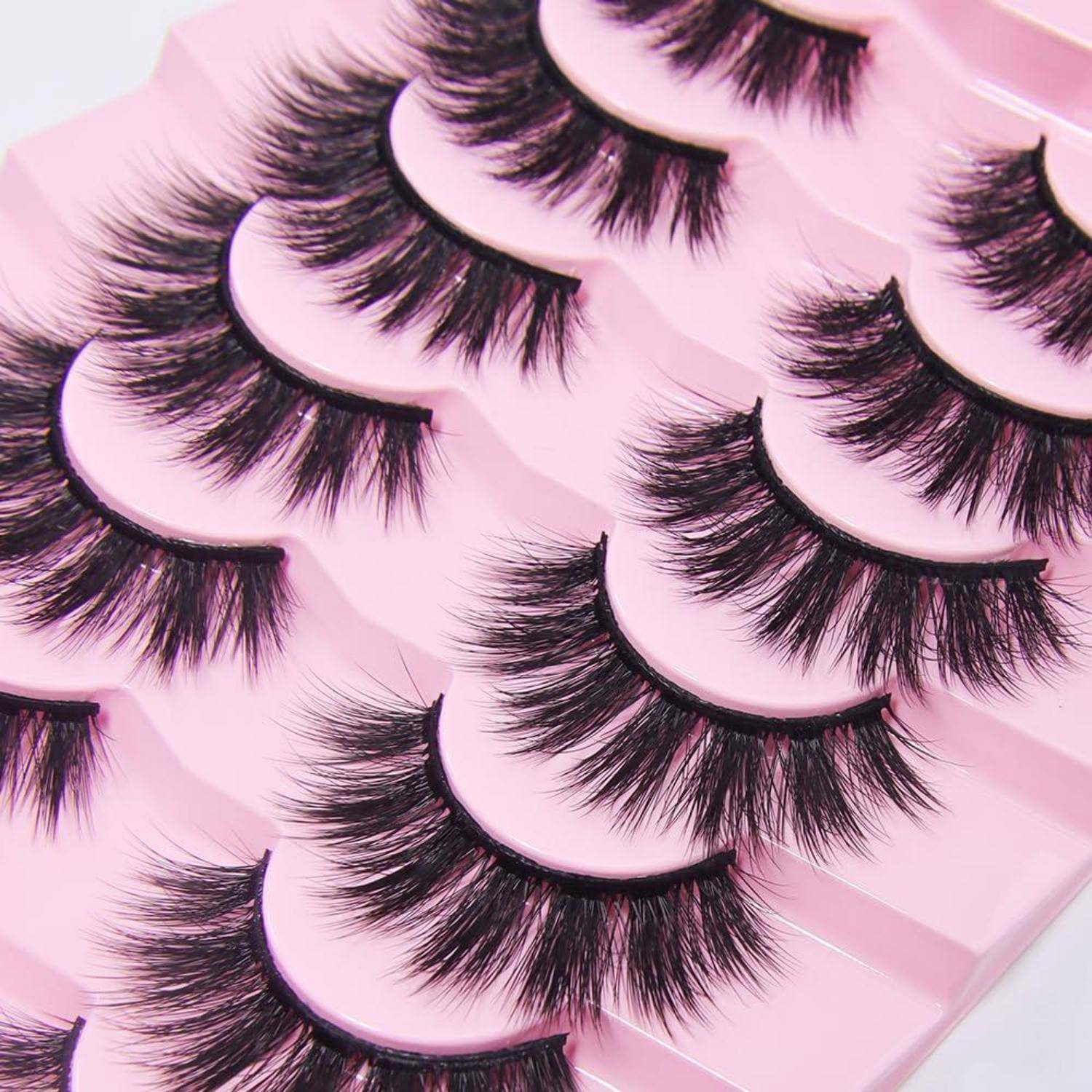 Gestapelte rosa Tabletts, auf denen mehrere Paare dicker schwarzer künstlicher Wimpern in einer Nahaufnahme-Produktfotografie präsentiert werden.