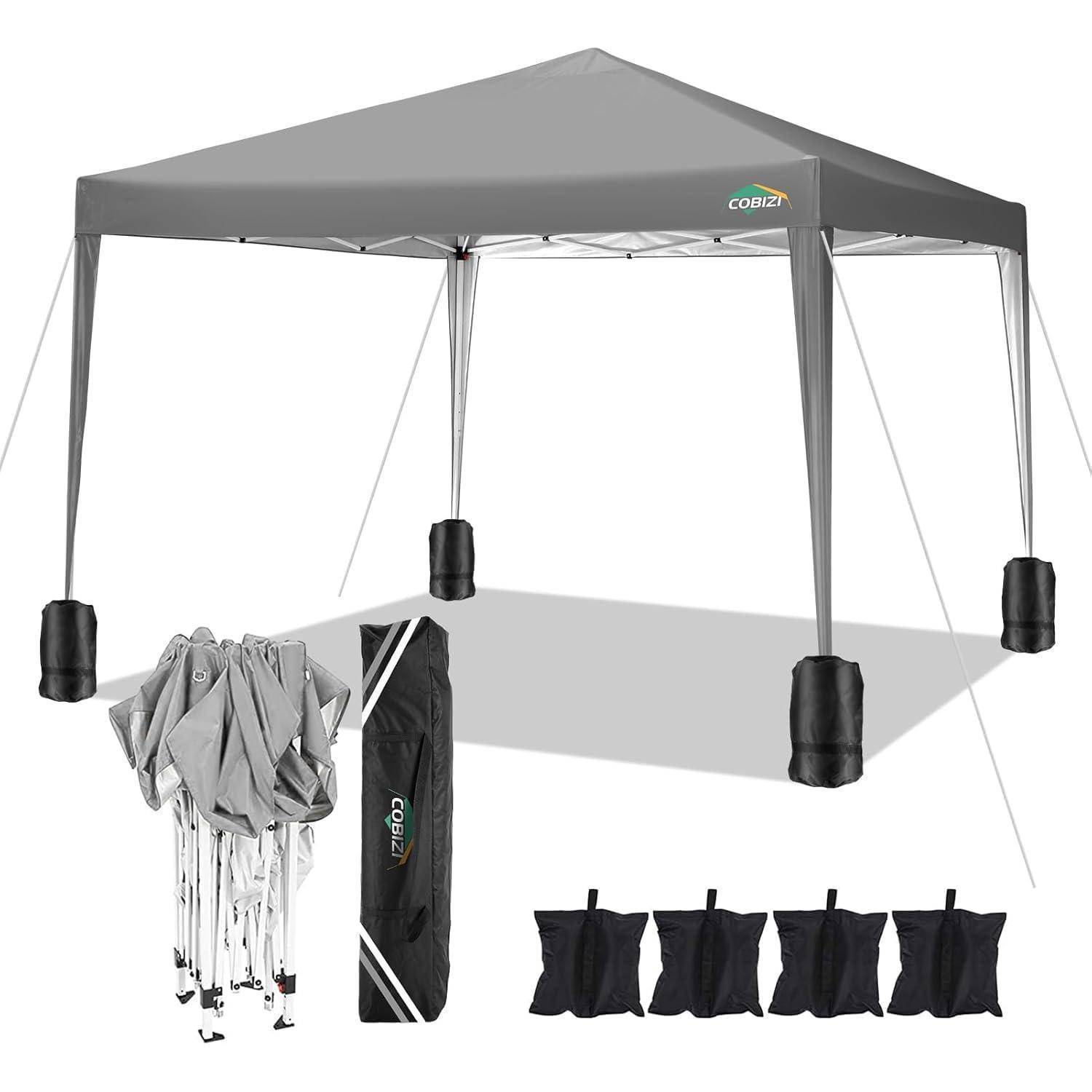 Grauweißes Pop-up-Pavillon-Zelt mit beschwerten Beintaschen und Tragetasche, gezeigt mit zusammengeklapptem Gestell und vier Sandsäcken, was auf ein tragbares Outdoor-Schutzdach-Set hindeutet