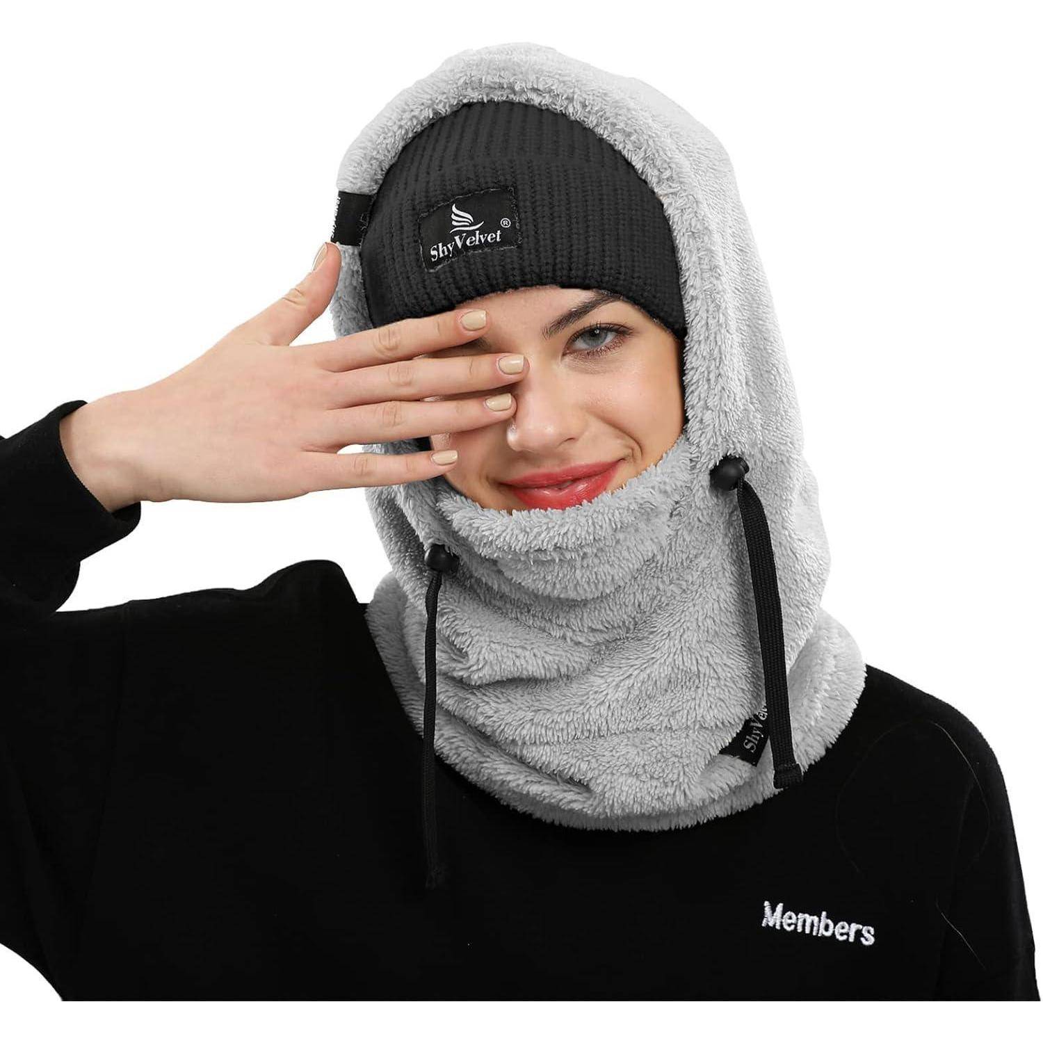 Person trägt eine graue Fleece-Kapuze und eine schwarze Beanie, bedeckt ein Auge mit einer Hand; schwarzes Sweatshirt auf weißem Hintergrund.
