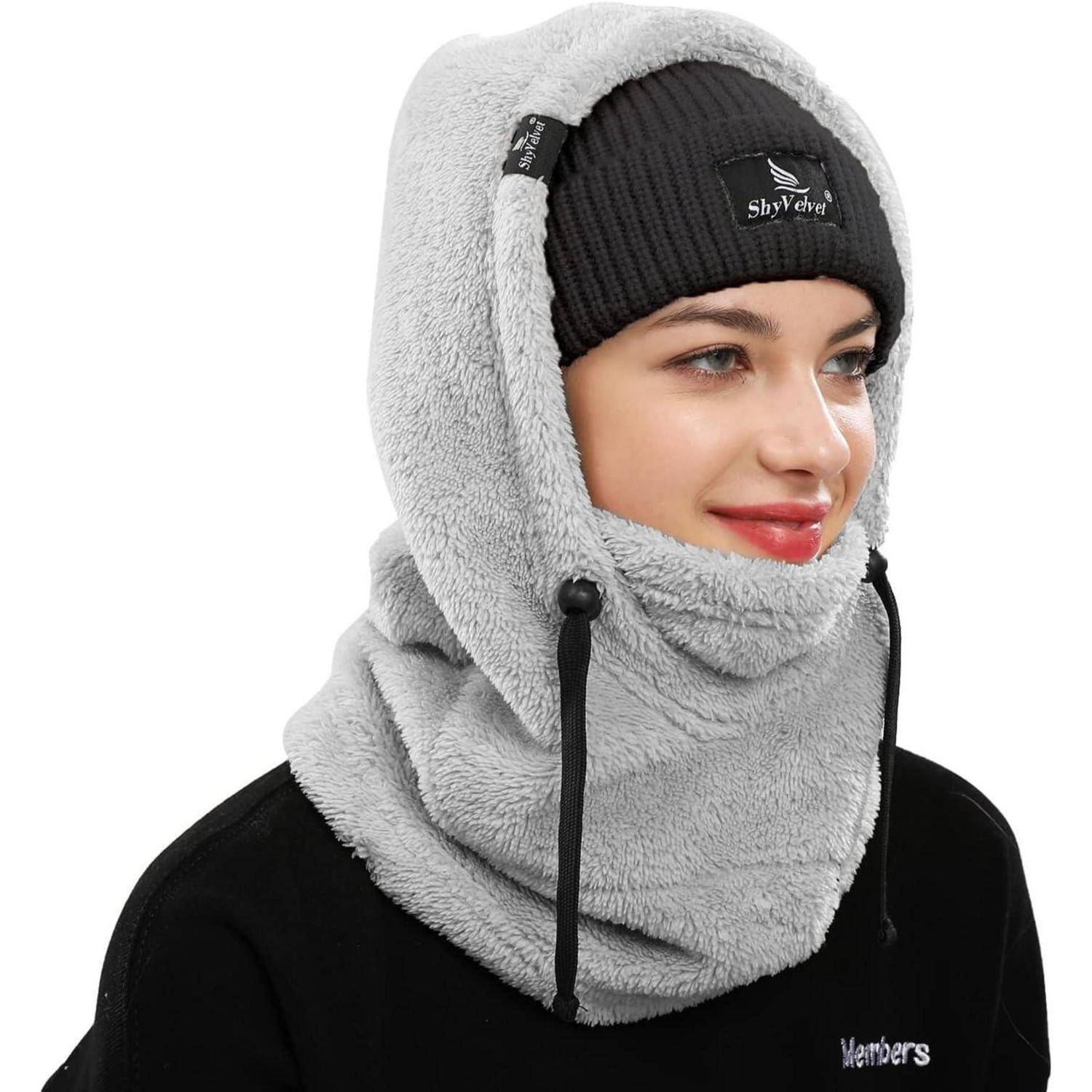 Frau, die eine graue Fleece-Sturmmaske und eine schwarze Beanie trägt, vor weißem Hintergrund gezeigt.