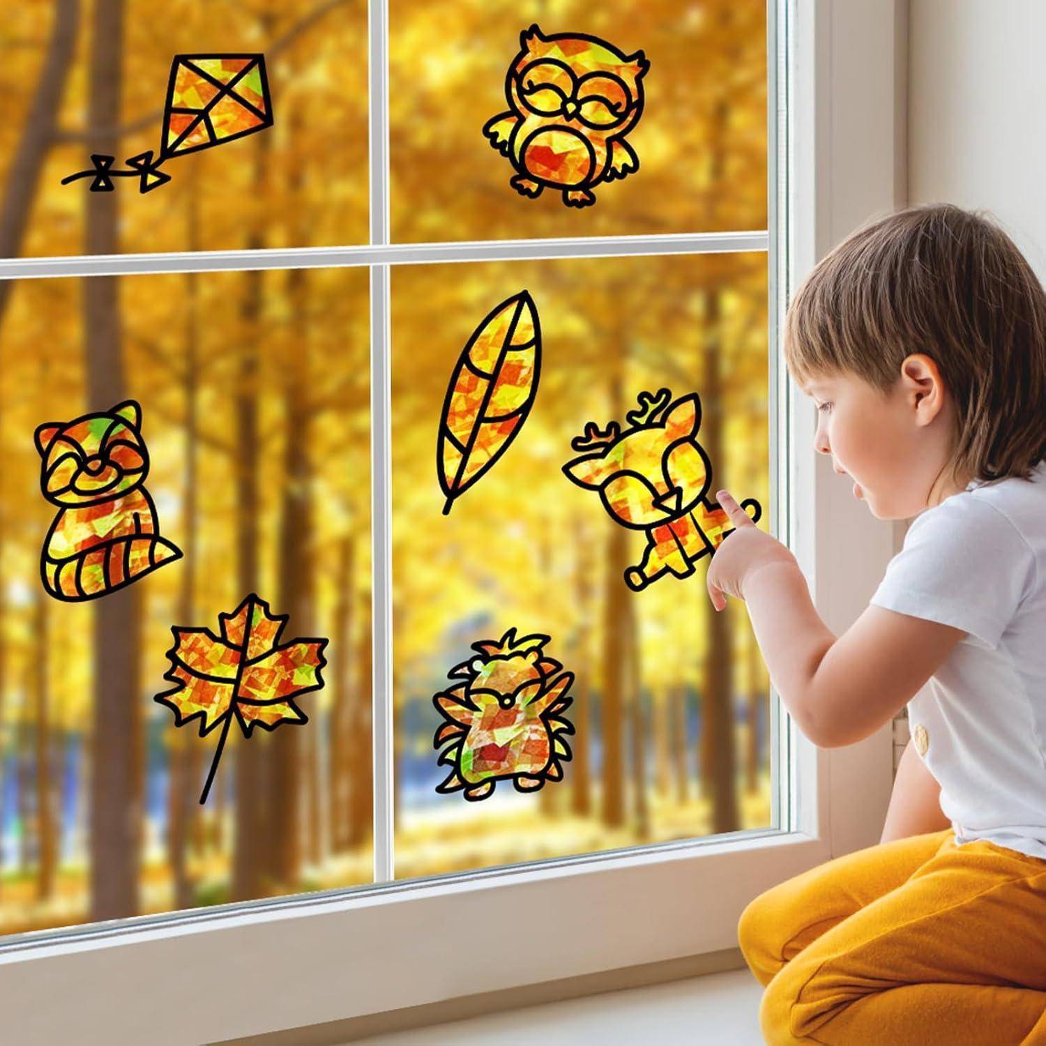 Ein Kind bringt eine Fensterfolie auf einer Scheibe an, die mit farbenfrohen herbstlichen Tieren, Blättern und Drachenfliegermotiven verziert ist.