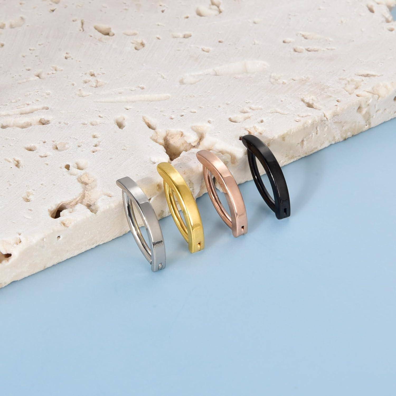 Vier minimalistische ovale Creolen aus Silber, Gold, Roségold und Schwarz auf einer hellblauen Oberfläche neben weißem Stein angeordnet.