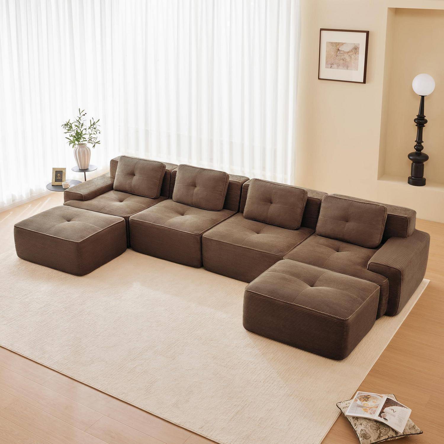 Braunes modulares Sektionssofa mit zwei Ottomanen auf einem beigen Teppich in einem hellen Wohnzimmer mit großen Vorhängen und minimaler Dekoration.