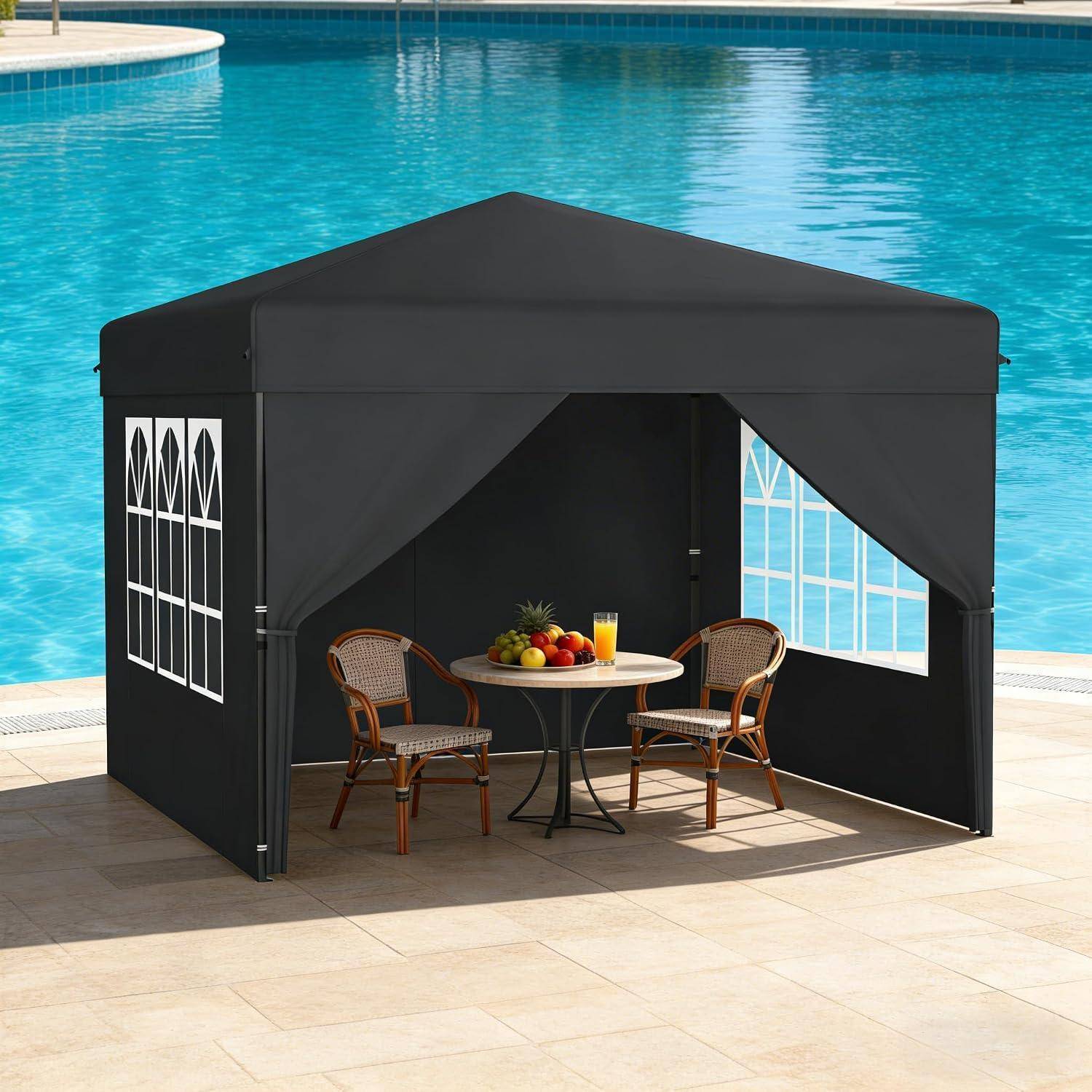 Schwarzes Pop-Up-Zelt neben einem Pool, mit zwei Rattanstühlen, einem kleinen runden Tisch, Obst und einem Getränk darin.