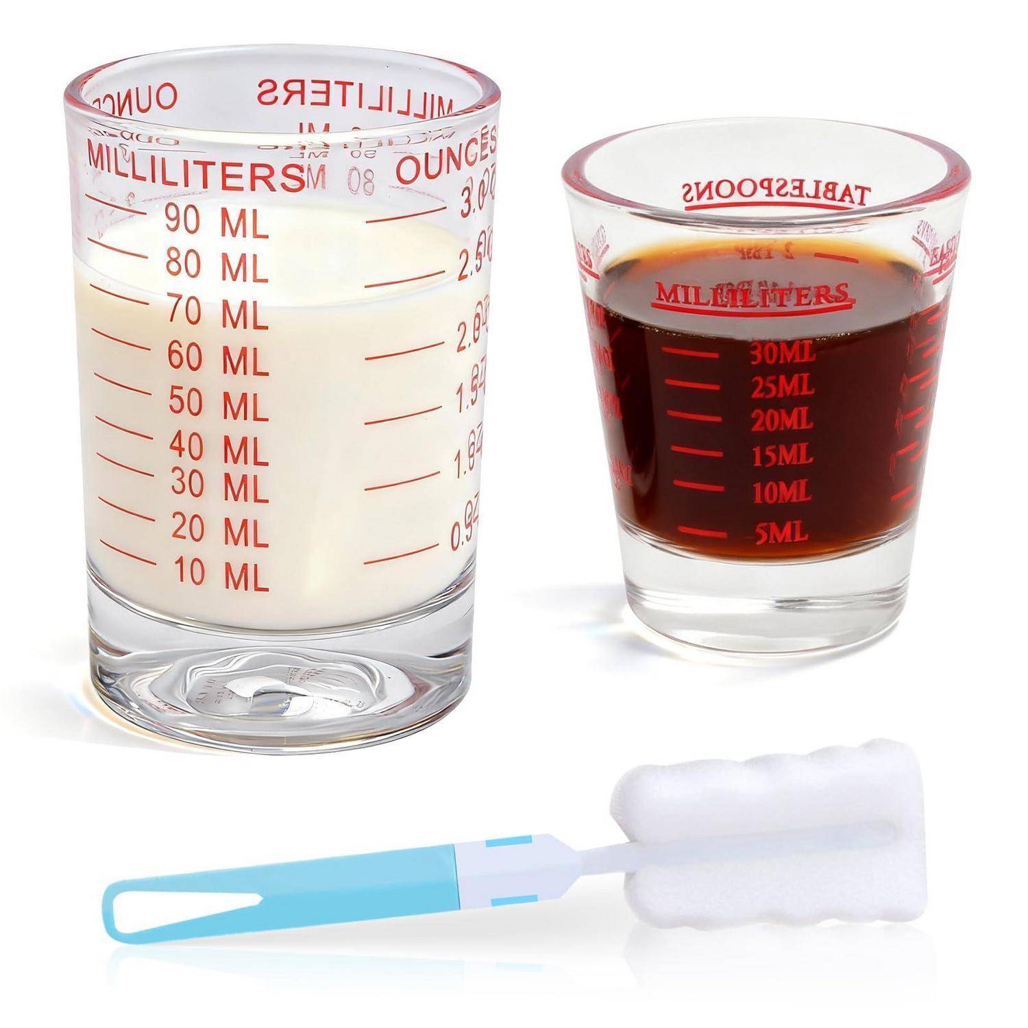 Drei klare Messbehälter mit roten Milliliter- und Unzen-Markierungen, einer mit Milch, einer mit dunkler Flüssigkeit, und ein Wattestäbchen mit blauem Griff.