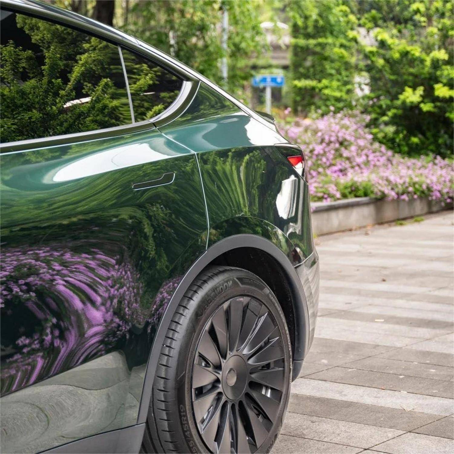 Rückseite eines dunkelgrünen SUV, der auf einem gepflasterten Weg geparkt ist, mit violetten Blumen und Grünanlagen, die in seinem glänzenden Lackwerk reflektiert werden.