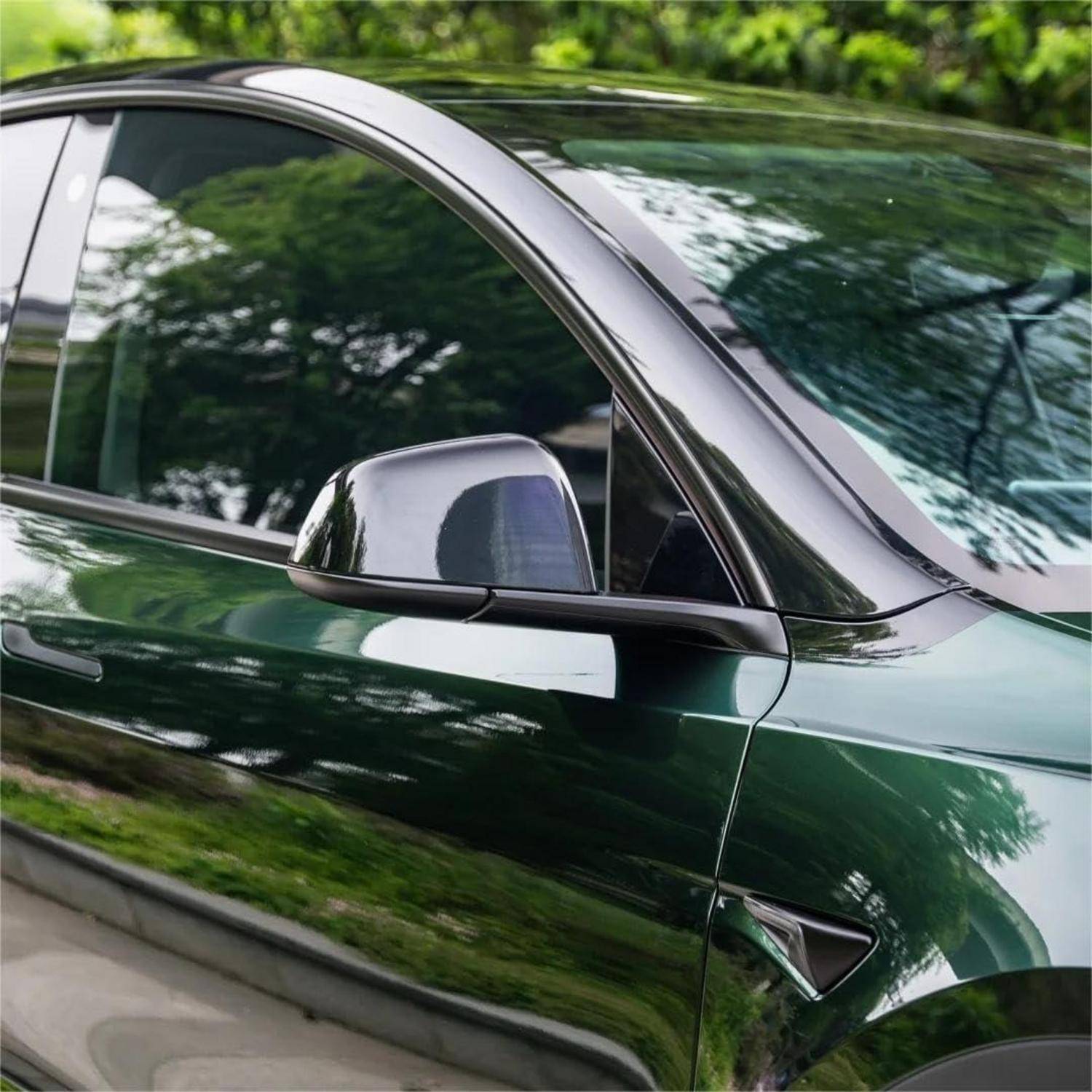 Nahaufnahme der Seite eines grünen Autos mit einem glänzenden Spiegel und getönten Fenstern, die Bäume und Himmel widerspiegeln.