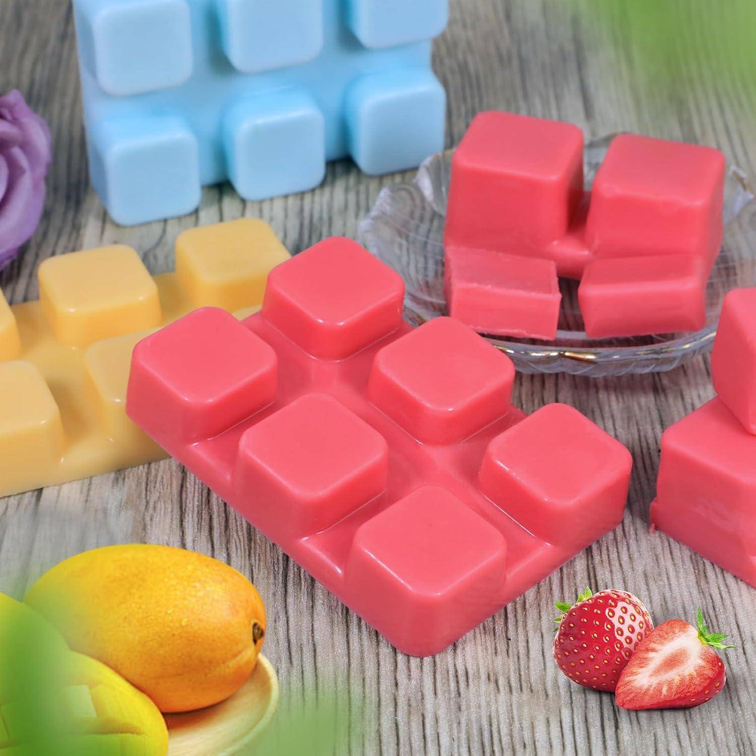 Bunte, fruchtduftende Wachsmelts in Ziegel- und Quadratform sind auf einer Holzoberfläche angeordnet, mit geschnittenen Erdbeeren und Mangos, die Düfte suggerieren.