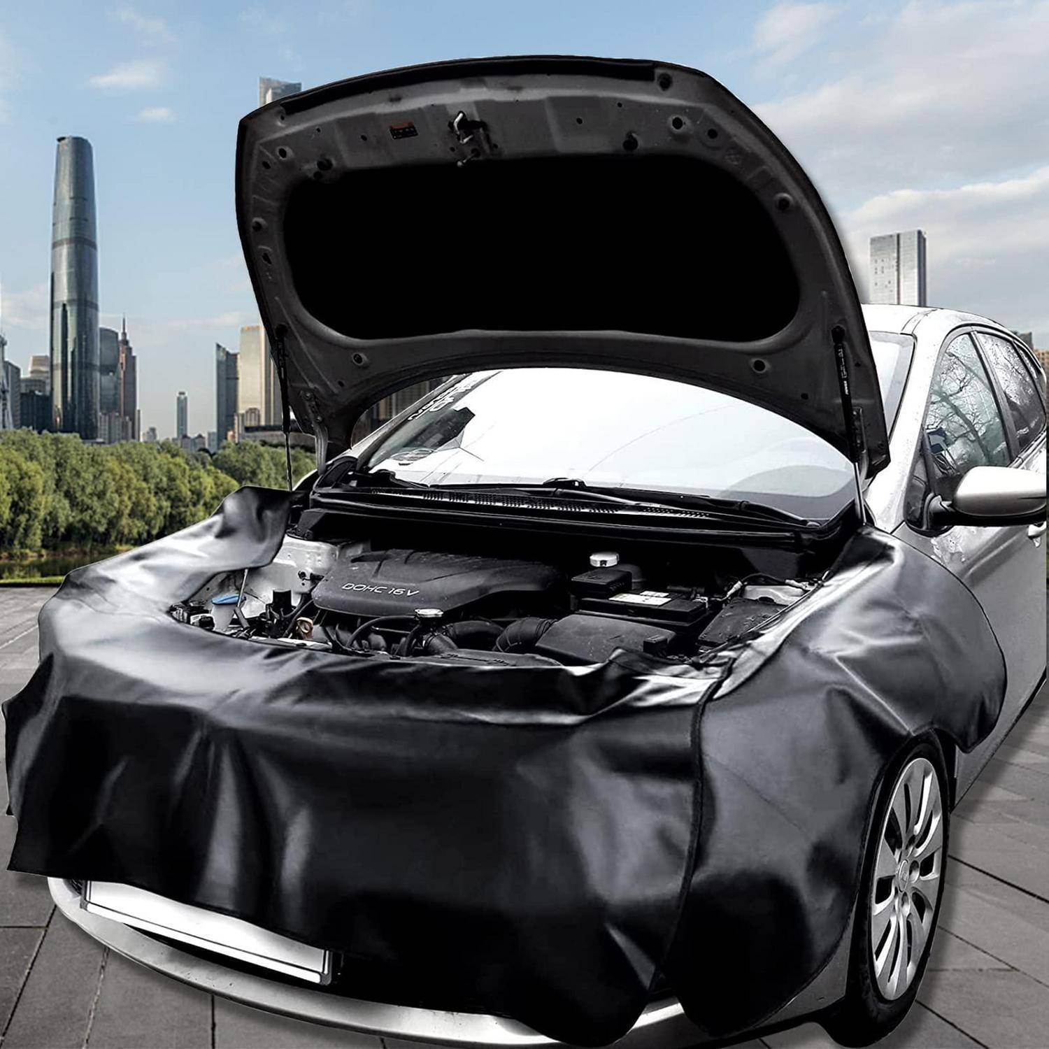 Auto mit offener Motorhaube und Front mit schwarzer Schutzfolie bedeckt, geparkt im Freien mit Stadtsilhouette im Hintergrund.