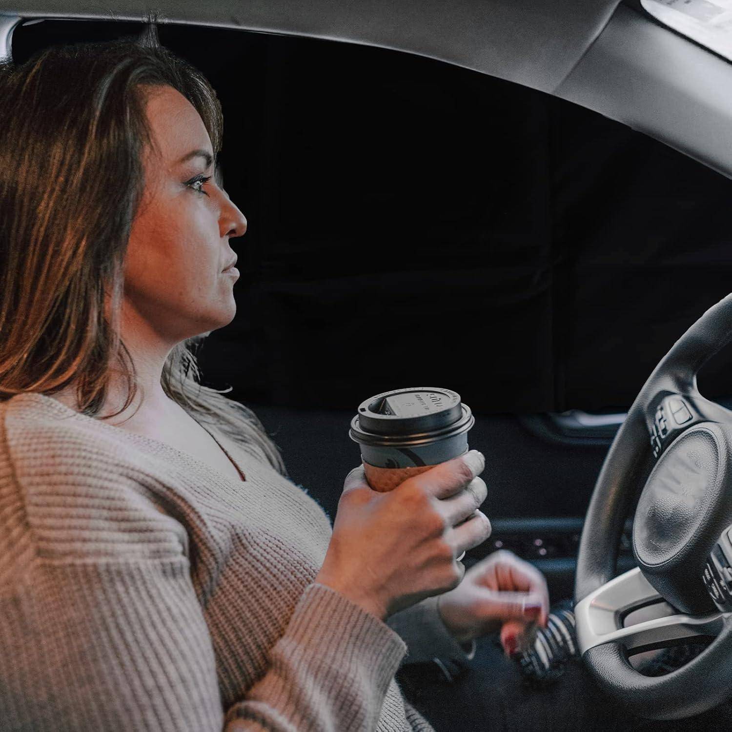 Frau, die auf dem Fahrersitz eines Autos sitzt, eine Kaffeetasse zum Mitnehmen hält und nach vorne schaut.