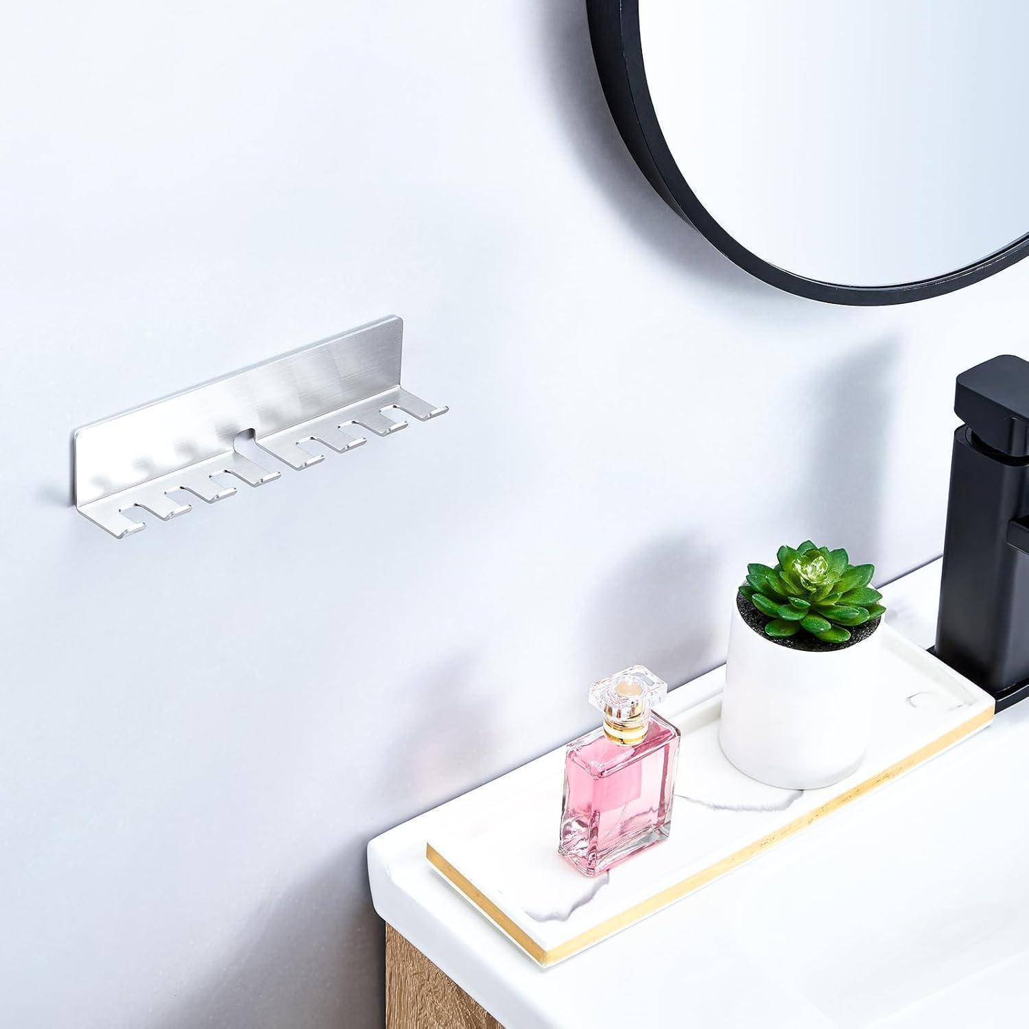Minimalistischer Badezimmerwaschbecken mit einer wandmontierten Hakenleiste, rundem Spiegel, weißem Tablett mit Parfüm und einer kleinen Topfpflanze Sukkulente.