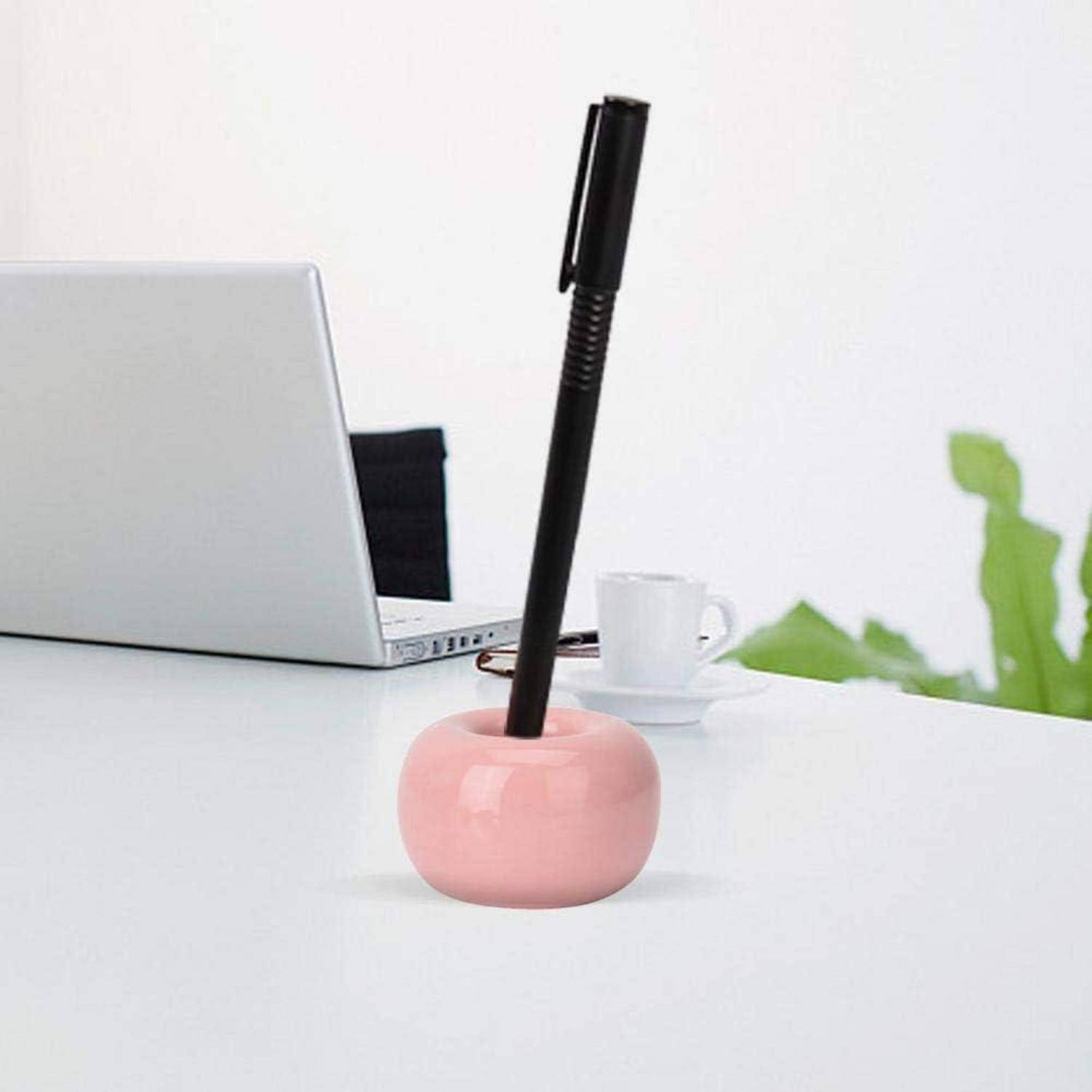 Rosafarbener Stifthalter auf einem weißen Schreibtisch mit einem schwarzen Stift; Laptop und Kaffeetasse verschwommen im Hintergrund.