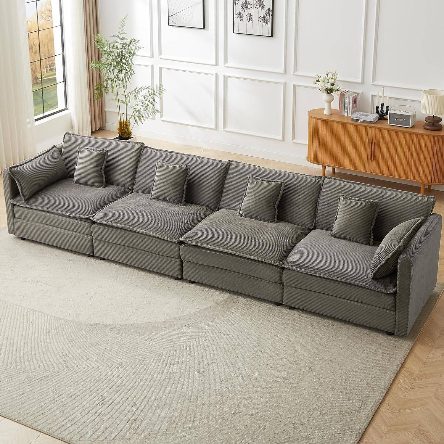 Graues modulares Sectional-Sofa mit mehreren Kissen in einem hellen, minimalistischen Wohnzimmer neben einem Sideboard und einem großen Teppich.
