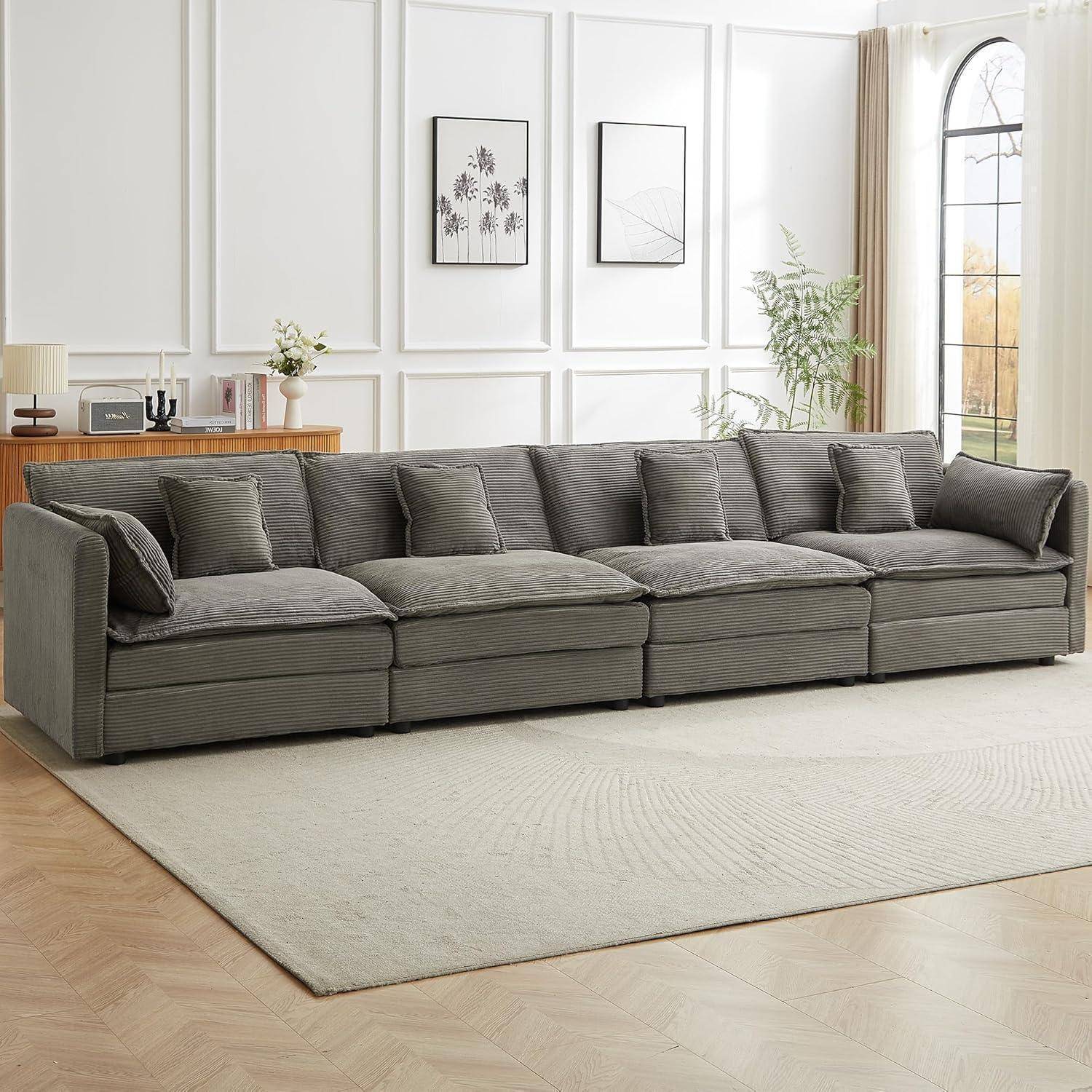 Graues Ecksofa mit Chaiselongue in einem hellen modernen Wohnzimmer, angeordnet auf einem hellen Teppich vor einer weiß getäfelten Wand mit Rahmenbildern und Pflanzen.