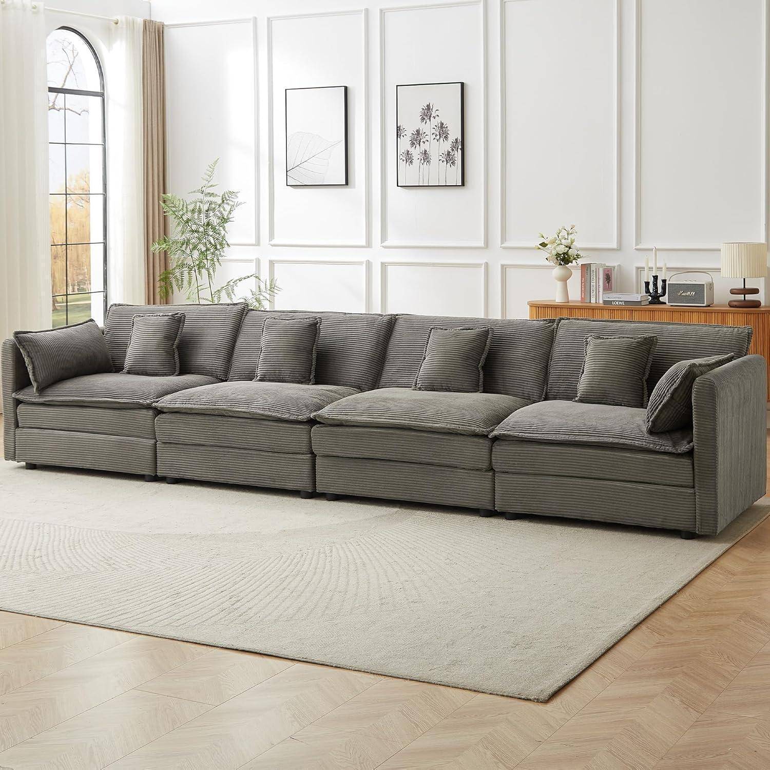 Großes graues Ecksofa mit mehreren Kissen in einem hellen Wohnzimmer mit Wandkunst, Fenster, Pflanzen und einem hellen Teppich.