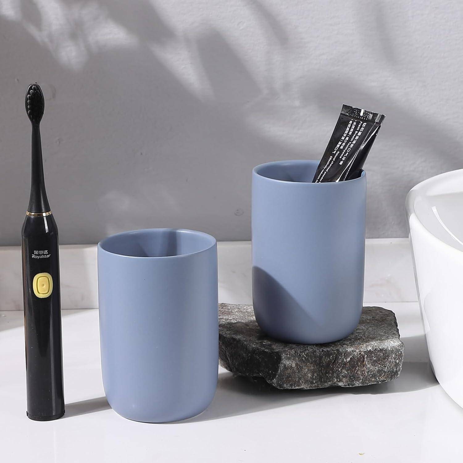 Badezimmer-Arbeitsplatte mit einer schwarzen elektrischen Zahnbürste und zwei hellblauen Bechern, von denen einer eine Zahnpastatube hält, auf einer Steinoberfläche.