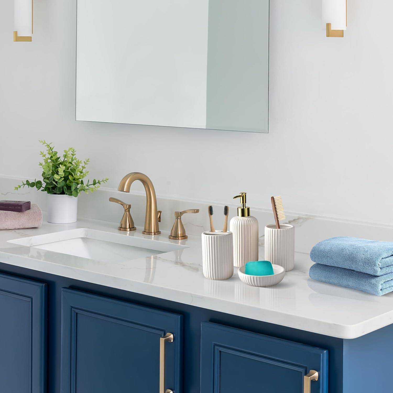 Modernes Badezimmerwaschtisch mit weißer Arbeitsplatte, blauen Schränken, goldfarbenen Armaturen und Beschlägen, Spiegel, Pflanze, Toilettenartikeln, Handtüchern und Seifenschale.