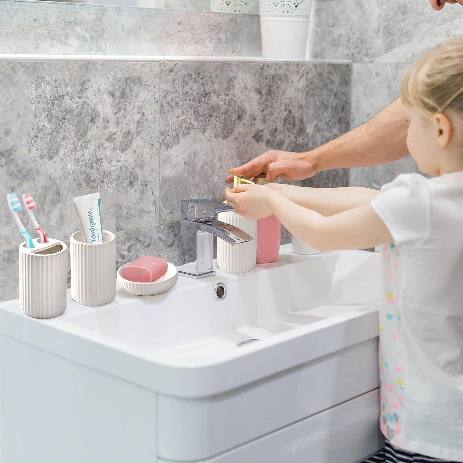 Ein Erwachsener hilft einem kleinen Mädchen, ihre Hände an einem Waschbecken im Badezimmer zu waschen, wobei Zahnbürsten und Zahnpasta neben dem Wasserhahn stehen.