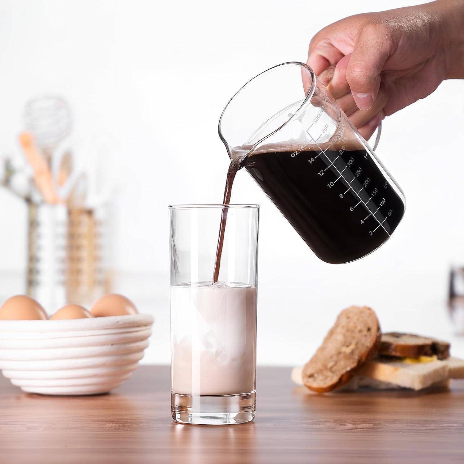 Eine Hand gießt schwarzen Kaffee aus einem Becher in ein Glas mit Milch auf einem Tisch, mit Eiern, Brot und Butter im Hintergrund.