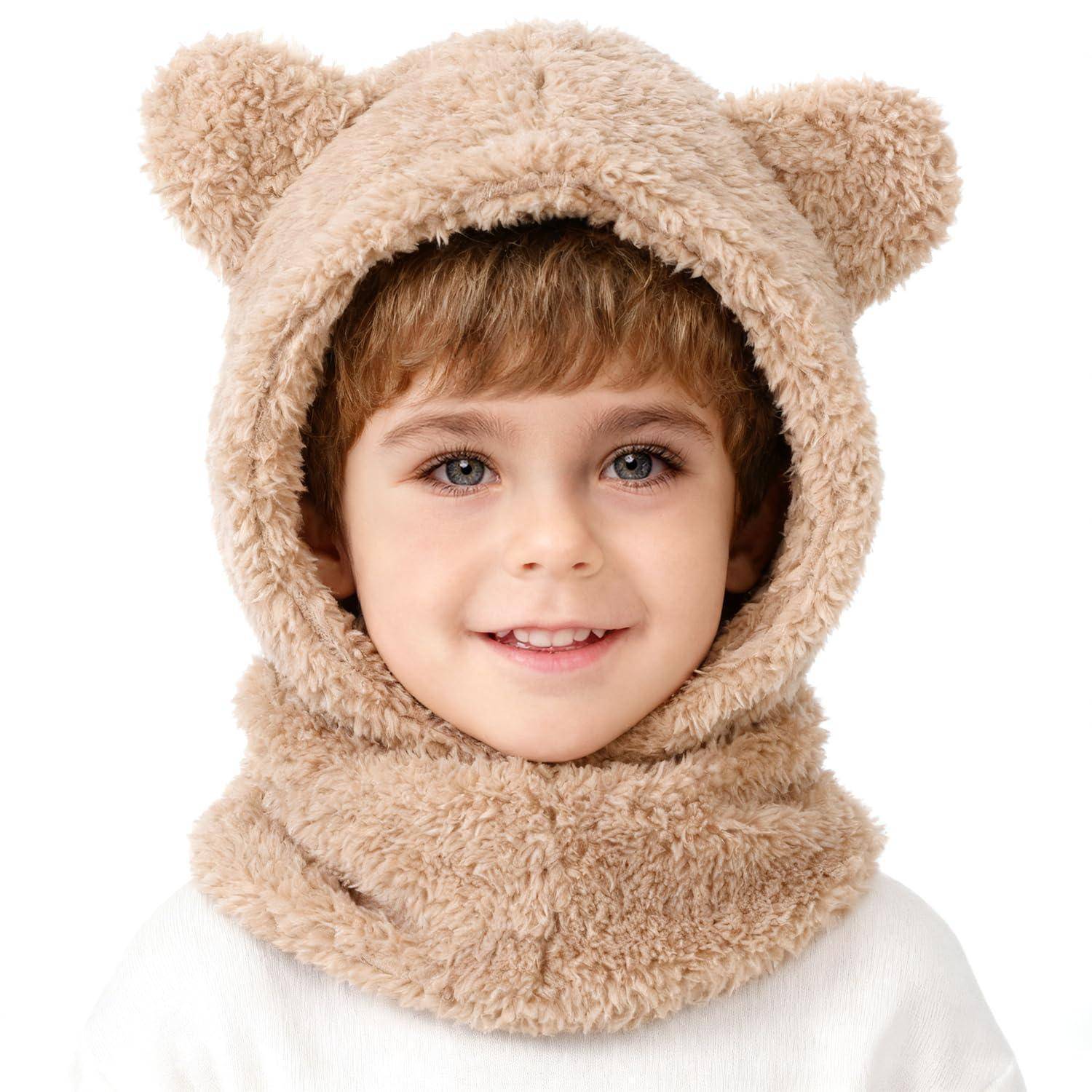 Junges Kind, das in einer flauschigen Teddybär-Kapuze und einem Schal lächelt, vor einem einfachen weißen Hintergrund posiert.