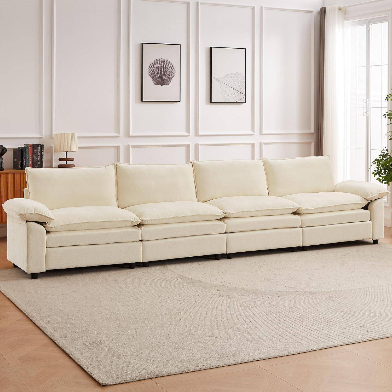 Ein cremefarbenes viersitziges Sofa in einem hellen, minimalistischen Wohnzimmer mit rahmenbildern an der Wand, einem Beistelltisch und einem großen Bereich Teppich.
