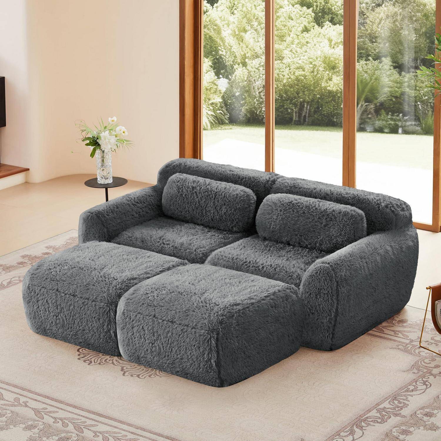 Graues, weiches modulares Ecksofa mit übergroßen Kissen in einem hellen Wohnzimmer neben großen Fenstern.
