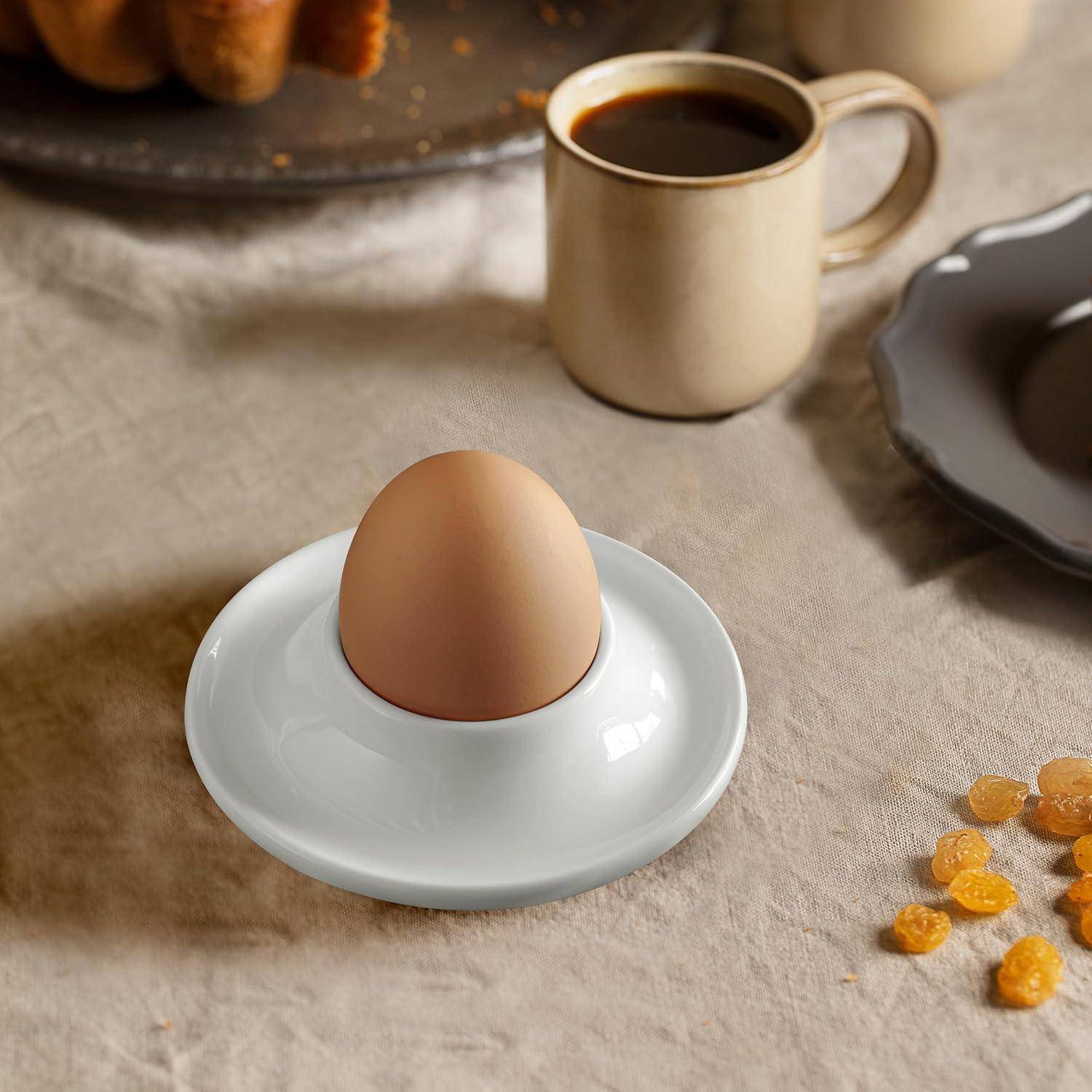 Ein weiches Ei in einem weißen Eierbecher mit einer Tasse Kaffee in der Nähe auf einem zum Frühstück gedeckten Tisch.