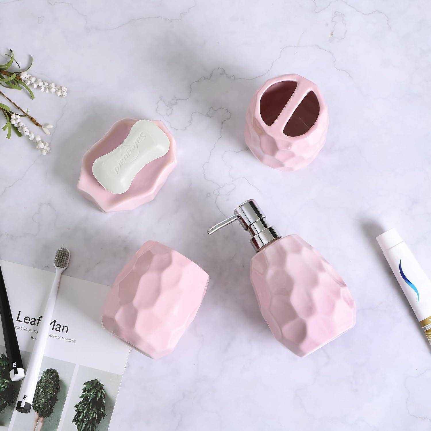 Rosa facettierter Badezimmer-Accessoireset auf einer Marmoroberfläche, einschließlich eines Seifenspenders, einer Seifenschale mit Stück, eines Zahnbürstenhalters, eines Bechers und einer Tube.