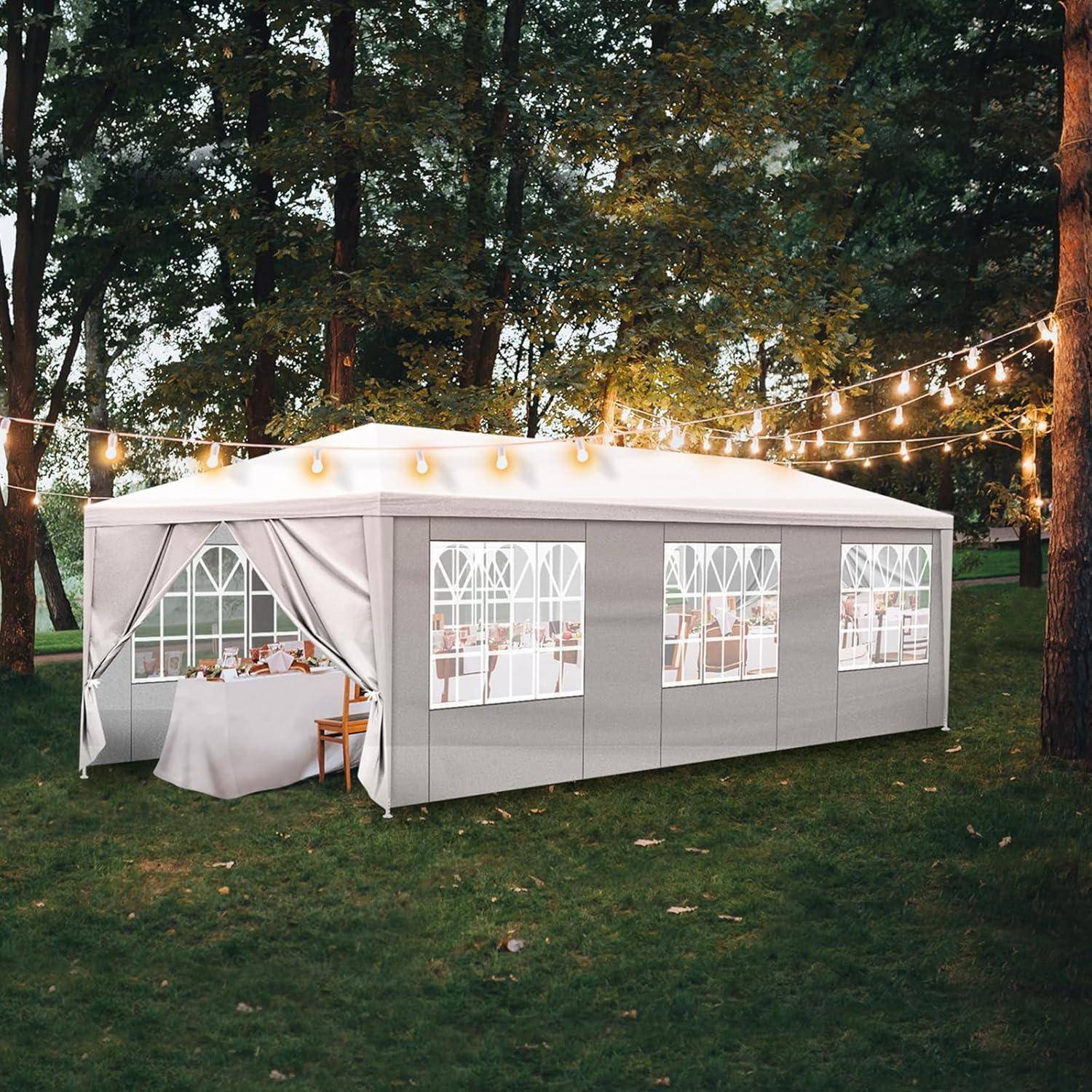 Eventloft im Freien mit weißem Baldachin, großen Fenstern und Lichterketten in einem bewaldeten Park, aufgebaut als Ess- oder Empfangsbereich.