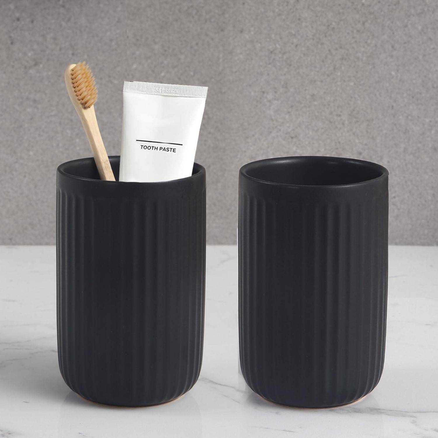 Zwei schwarze gerippte Badezimmergläser auf einer Marmoroberfläche; eines enthält eine Zahnbürste und eine Zahnpastatube mit der Aufschrift „TOOTH PASTE