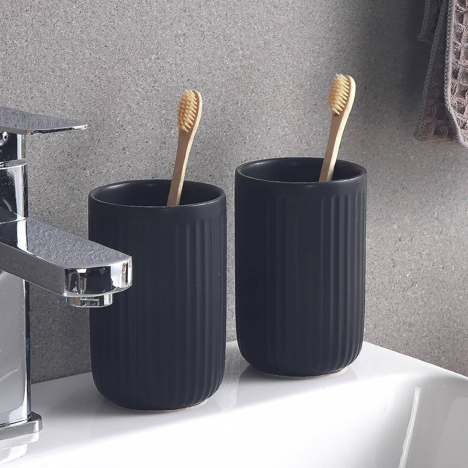 Zwei schwarze gerippte Zahnbürstenbehälter mit Bambus-Zahnbürsten neben einem verchromten Badezimmerwasserhahn auf einem weißen Waschbecken.