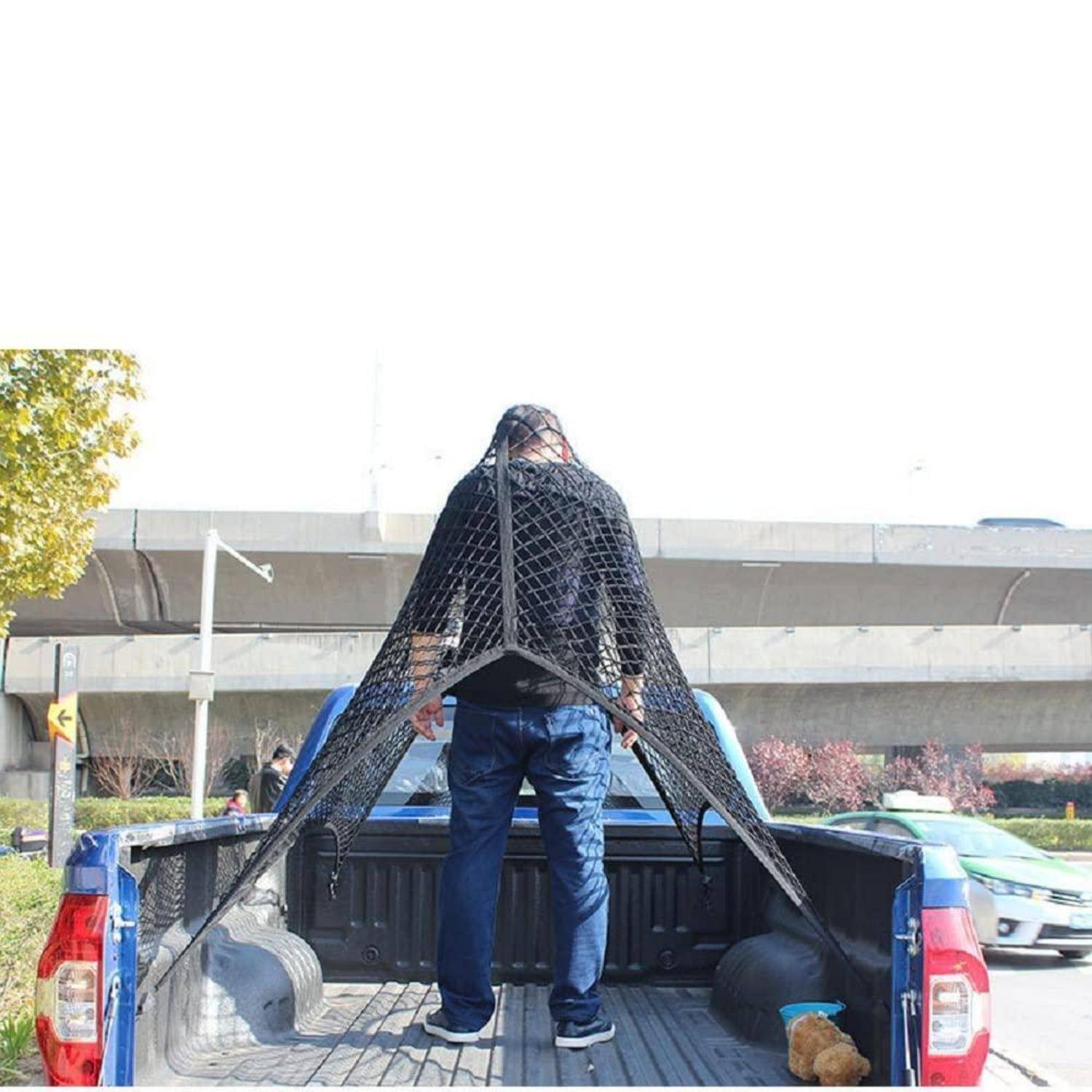 Ein Mann steht in der Ladefläche eines Pickup-Lastwagens unter einer großen schwarzen netzartigen kegelförmigen Abdeckung im Freien in der Nähe einer Autobahnüberführung.