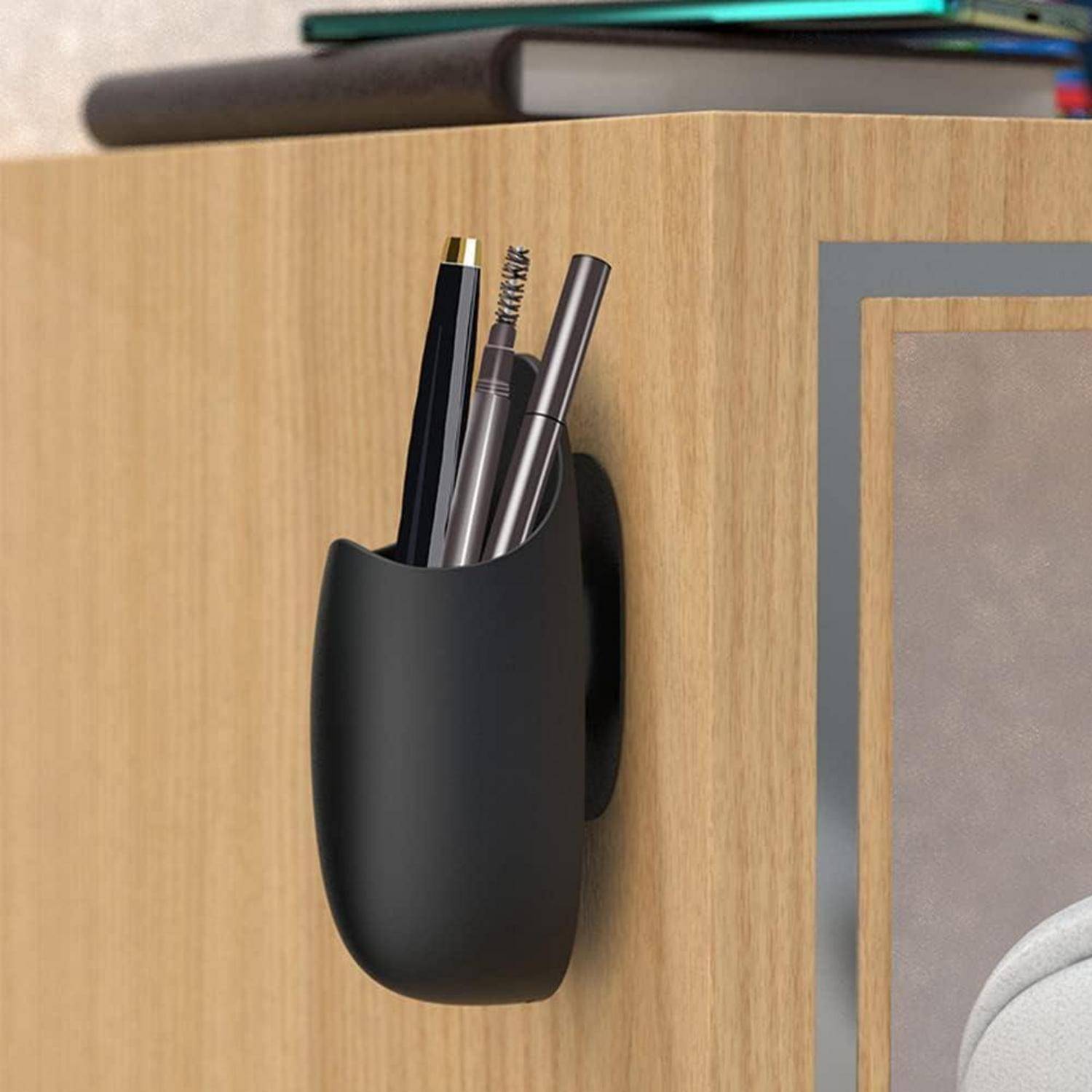Schwarzer, an der Wand angebrachter Stifthalter mit einem Stift, Bleistift und Pinsel an einer Holzschranktür.