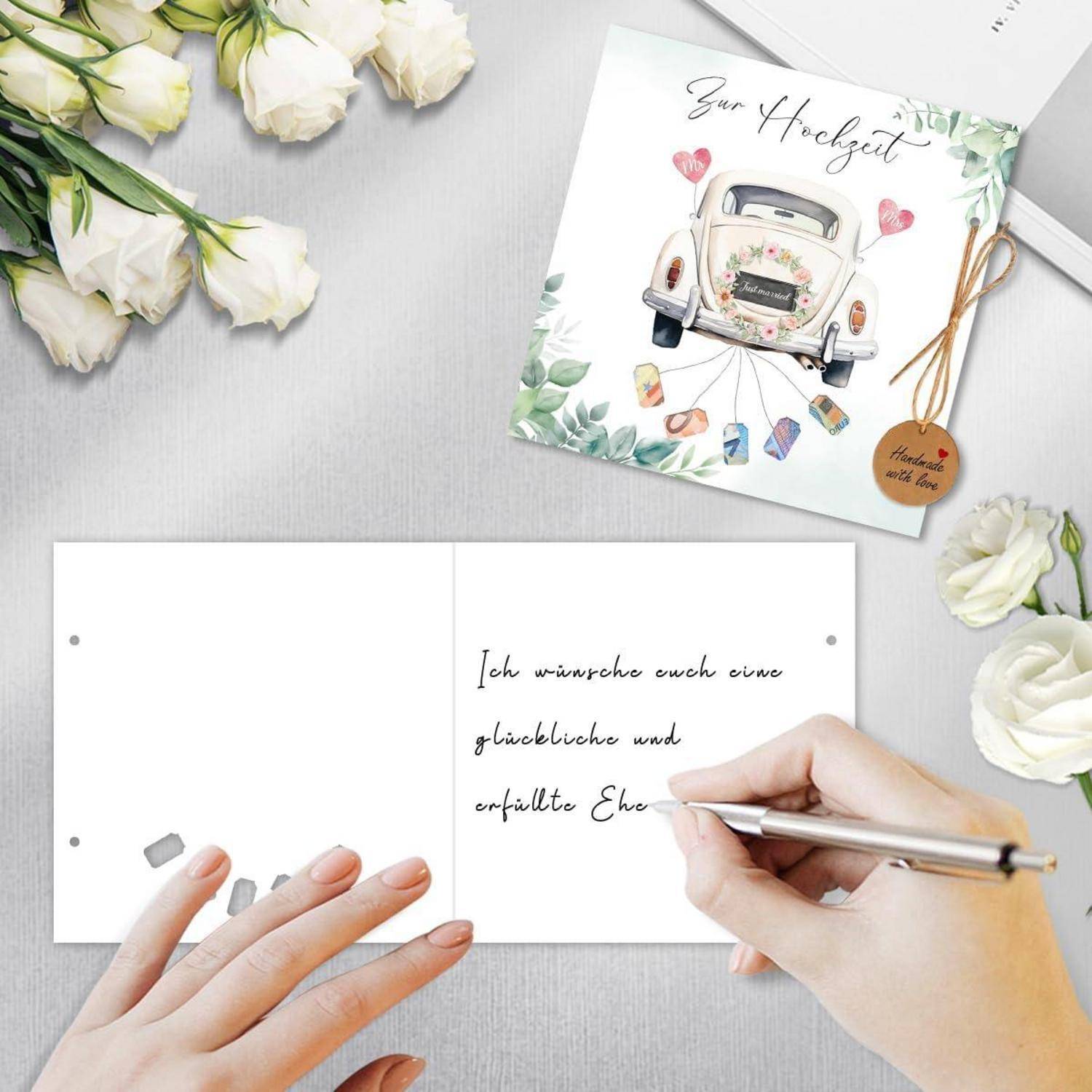 Eine Person schreibt handschriftlich einen deutschen Hochzeitsgruß in eine leere Karte neben einer dekorierten Karte, auf der „Zur Hochzeit