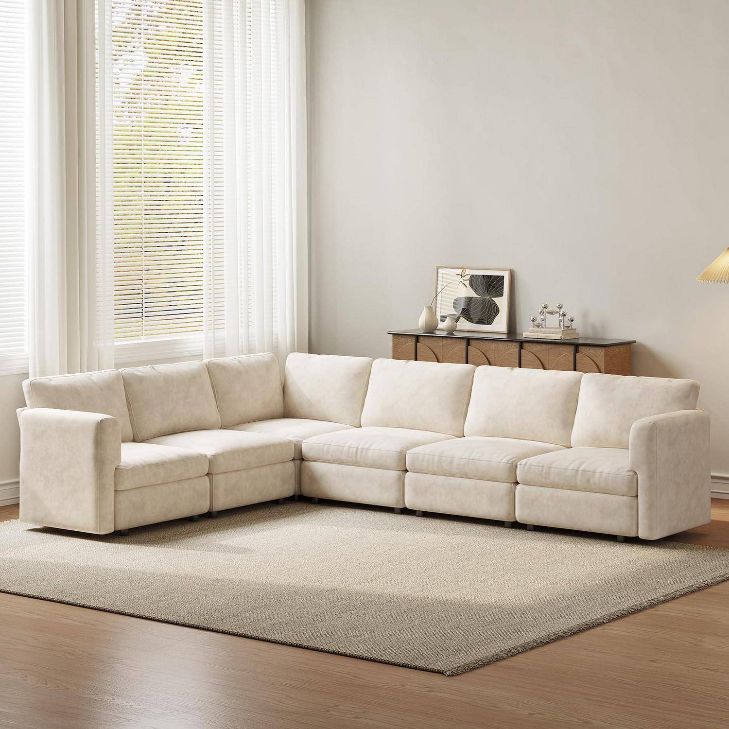 Beige L-förmiges Ecksofa in einem hellen Wohnzimmer mit einem Teppich, einem Sideboard und einem großen Fenster.