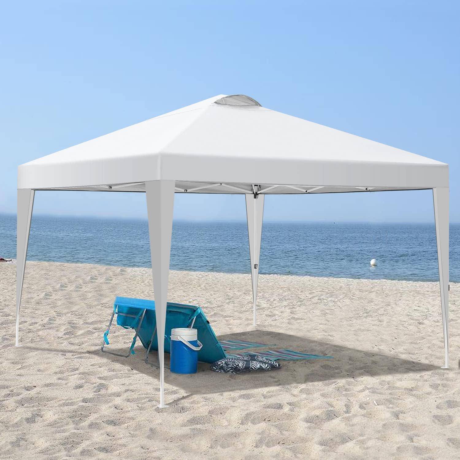 Weißes Strandzelt mit Vordach auf sandigem Ufer mit zwei blauen Stühlen, einer Kühlbox und Handtüchern, mit Blick auf den Ozean unter klarem Himmel.