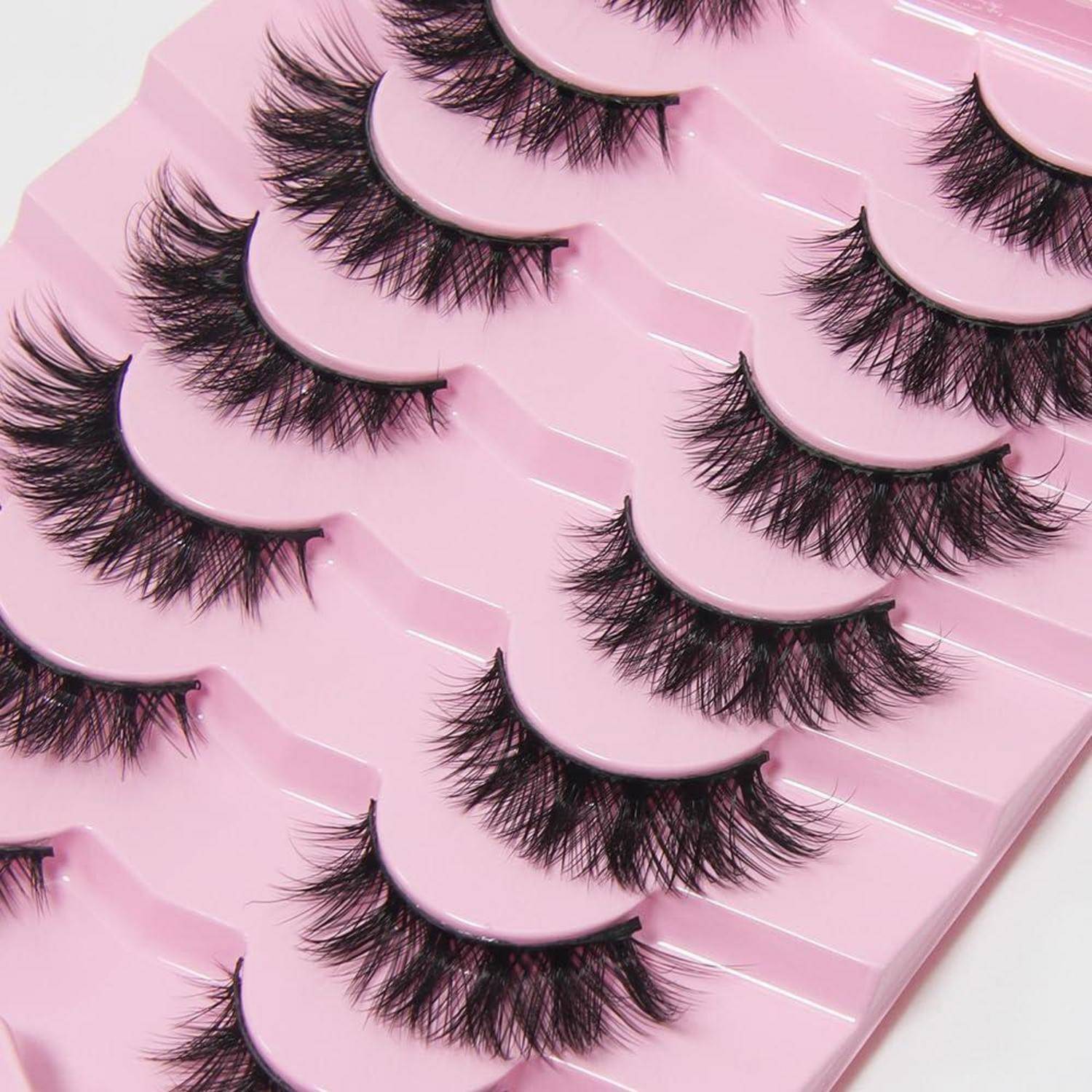 Mehrere Paare von künstlichen Wimpern, die in Reihen auf einem rosa Anzeigetablett angeordnet sind.