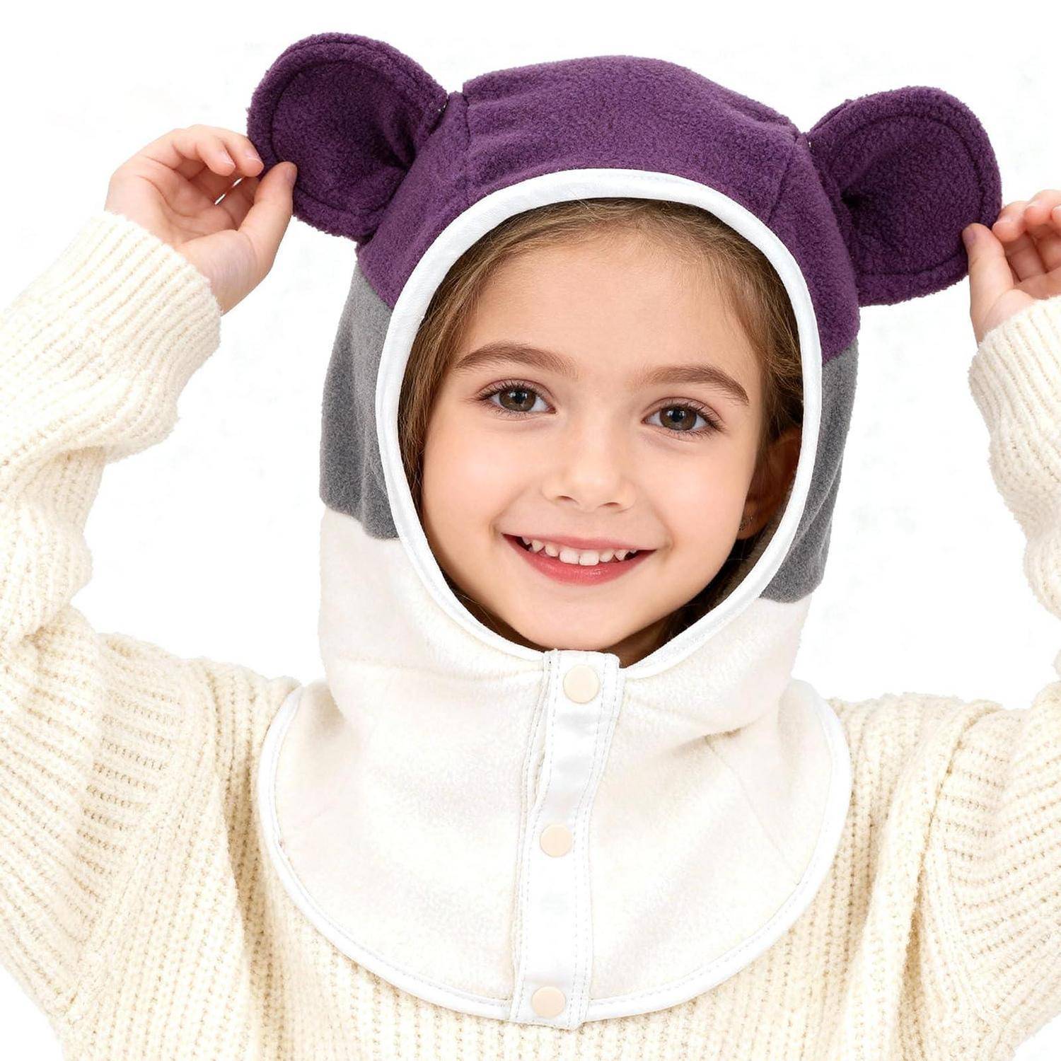 Lächelndes Kind, das ein weißes Kostüm mit Kapuze und violetten bärenähnlichen Ohren trägt, hält die Kapuze vor einem einfachen weißen Hintergrund hoch.