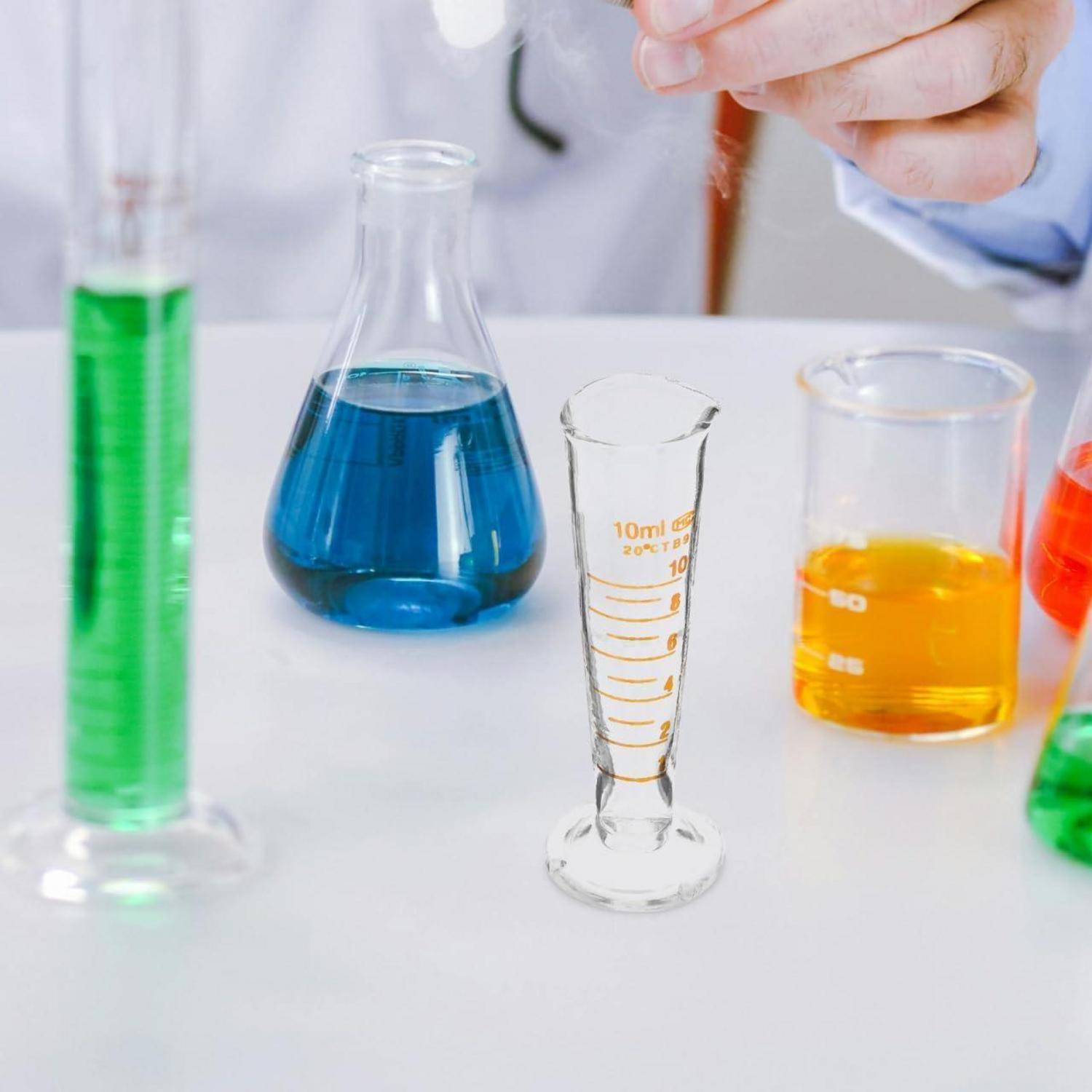 Laborglasware mit farbigen flüssigen Chemikalien, einschließlich eines blauen Kolbens, grüner und orangefarbener Bechergläser und eines Messzylinders auf einem Labortisch.
