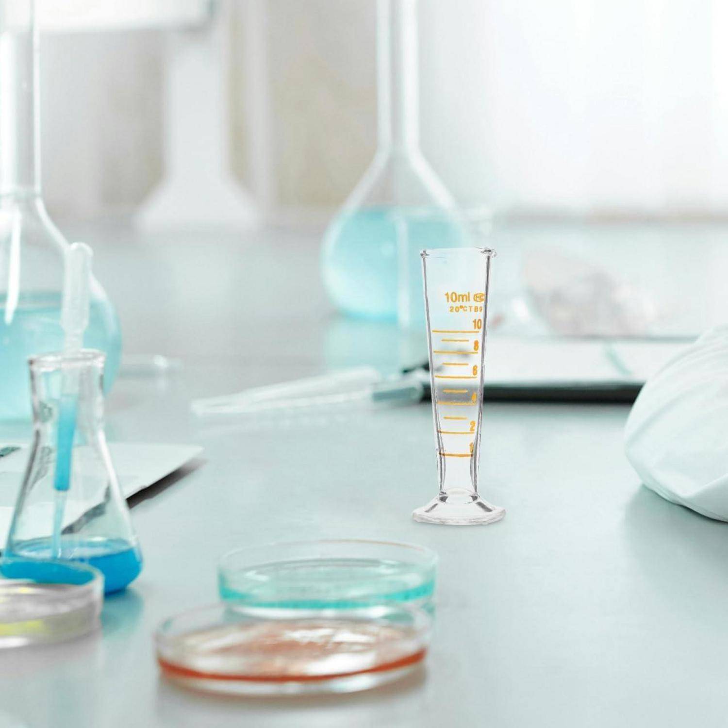 Laborglasware mit Petrischalen und Bechergläsern auf einer Werkbank, einschließlich eines 10-ml-Messzylinders in der Mitte.