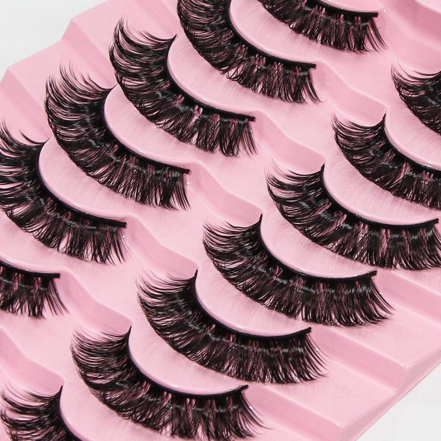 Nahaufnahme mehrerer dicker künstlicher Wimpern, die in Reihen auf rosa Verpackungstabletts angeordnet sind.