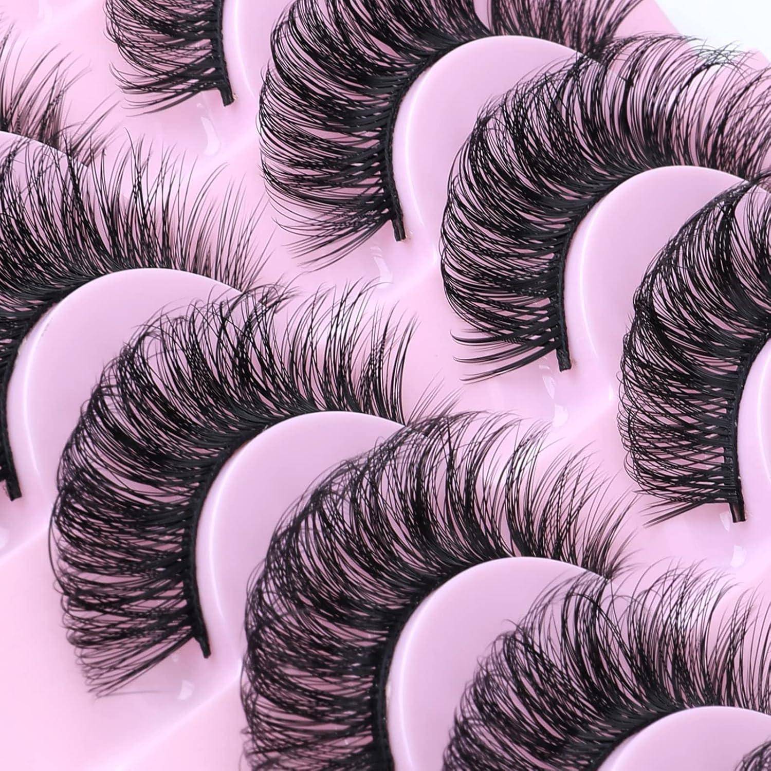 Mehrere Paare lange schwarze künstliche Wimpern auf rosa Kunststoffplatten angeordnet, überlappend in einer detaillierten Produktpräsentation.