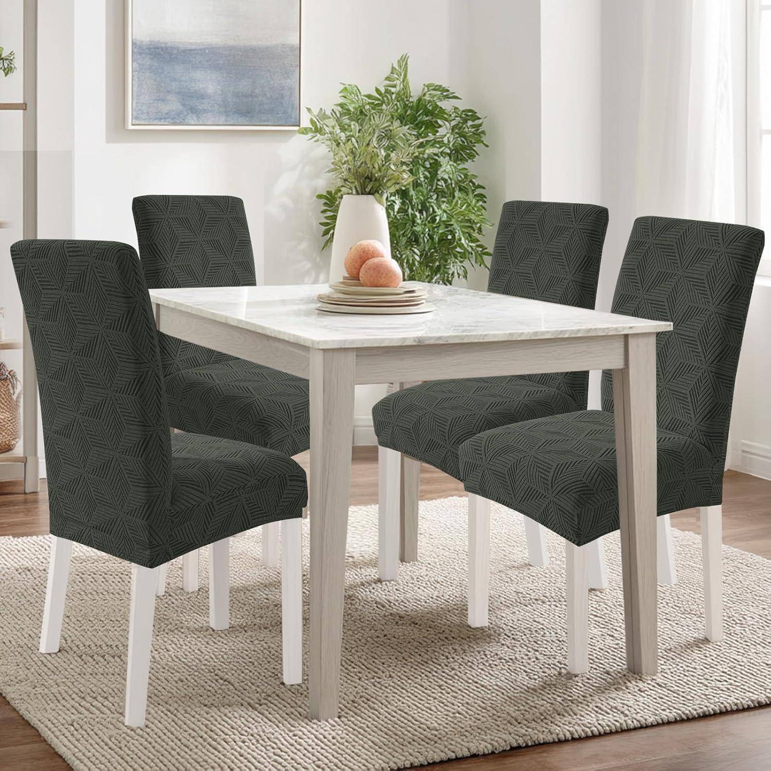 Vier dunkel gemusterte gepolsterte Esszimmerstühle um einen hellholzigen quadratischen Tisch in einem hellen modernen Esszimmer mit Teppich und Pflanzen.