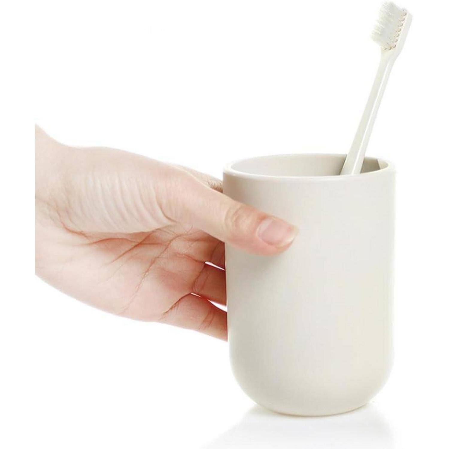 Hand, die eine weiße Tasse mit einer Zahnbürste darin auf einem einfachen weißen Hintergrund hält.